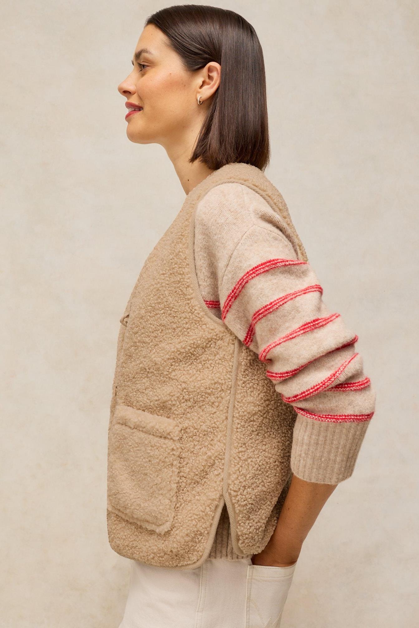 A woman wearing a cosy, neutral-coloured fleece gilet over a striped sweater.
