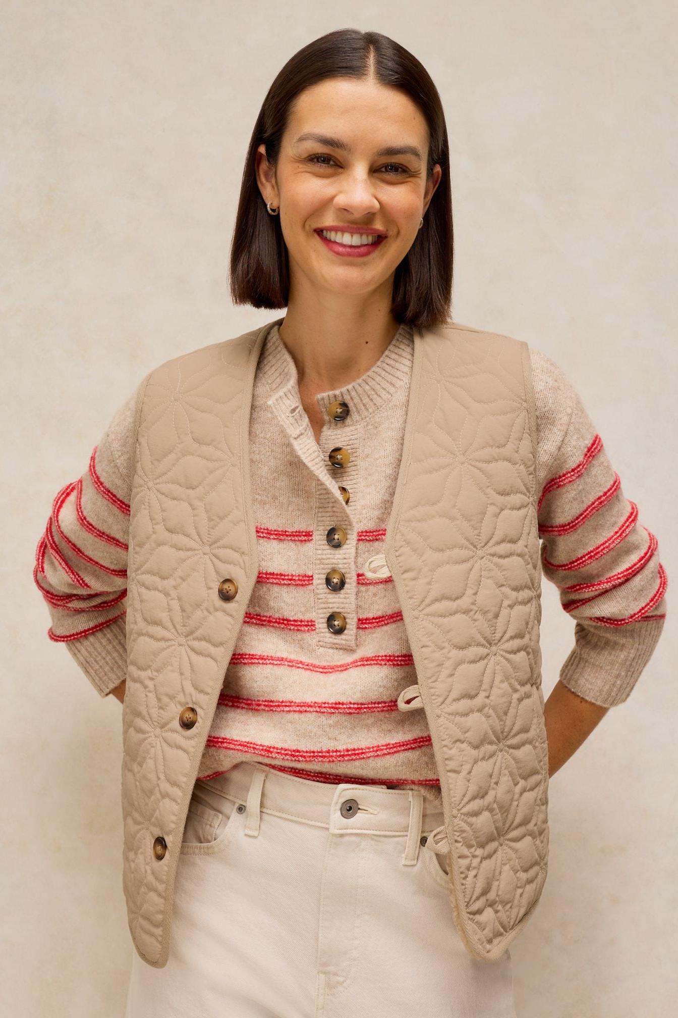 A woman smiling while wearing a neutral colour women's gilet over a striped sweater.