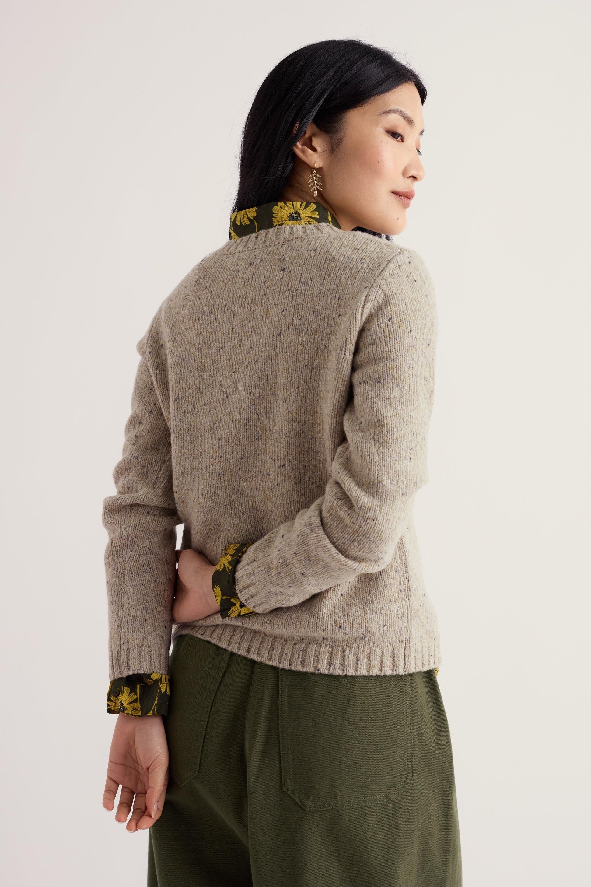 A woman wearing a textured neutral wool jumper over a floral shirt against a plain background.