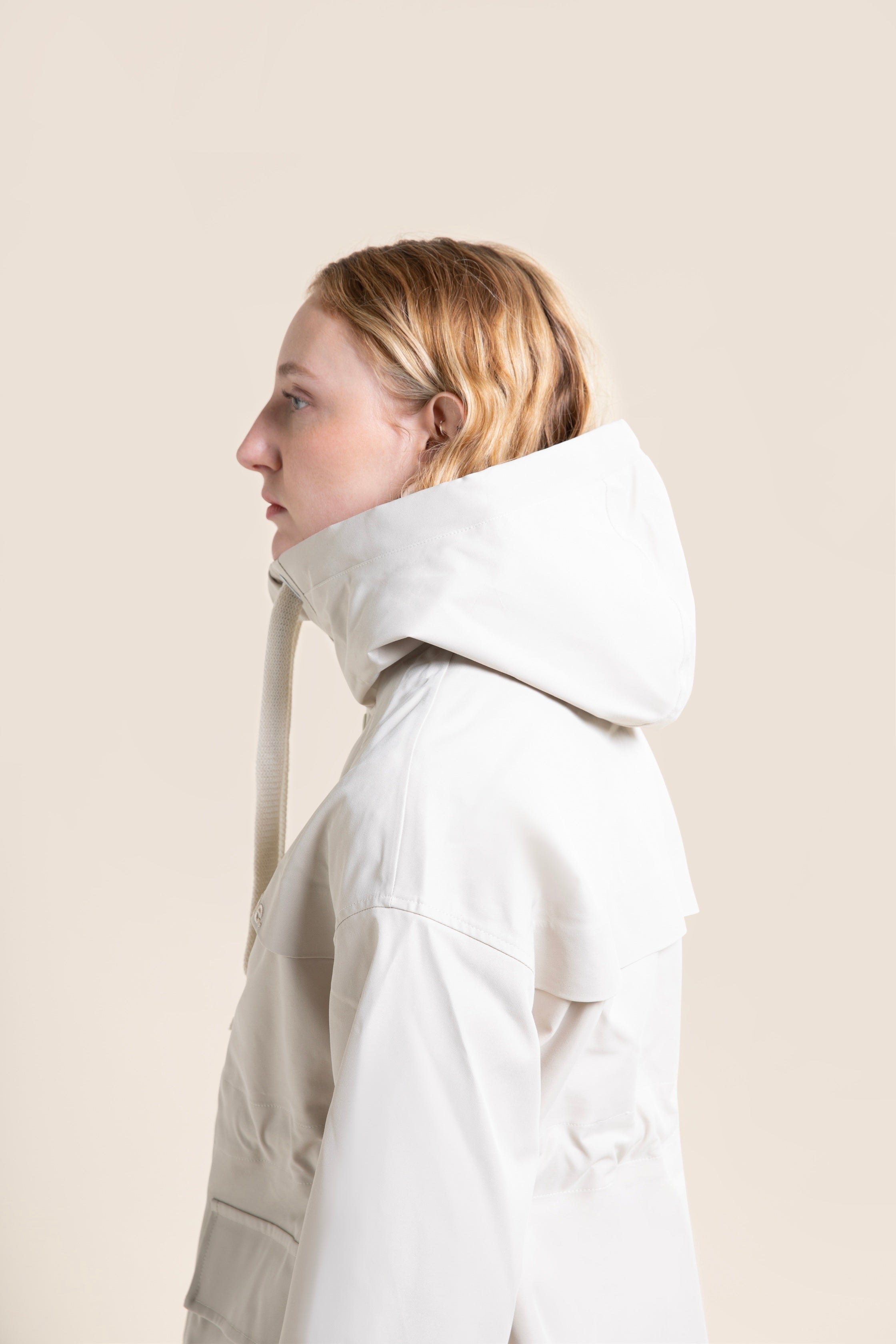 A woman wearing a stylish off-white waterproof parka coat against a neutral beige background.