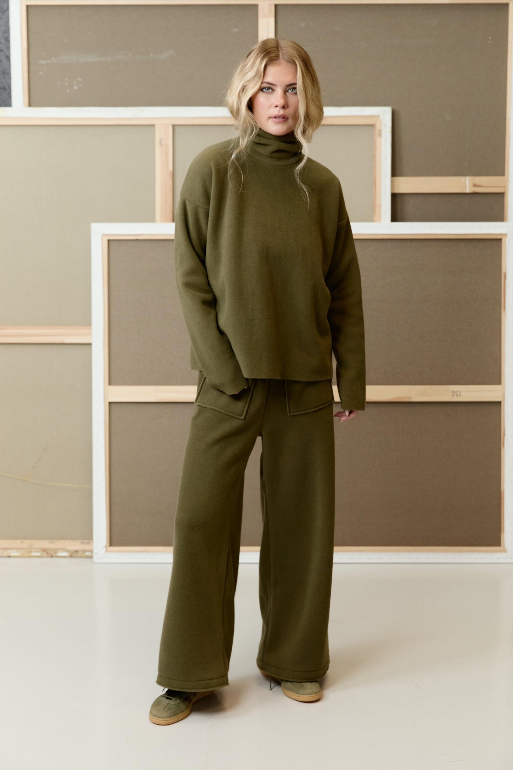 A woman wearing a matching olive green sustainable fleece turtleneck and wide-leg trousers from Henriette Steffensen.