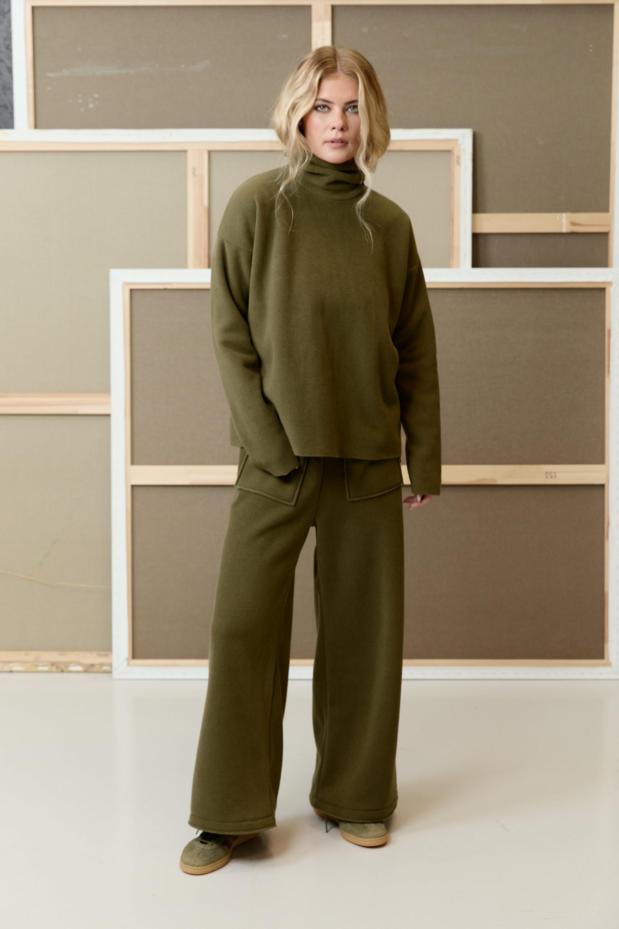 A woman wearing a matching olive green sustainable fleece turtleneck and wide-leg trousers from Henriette Steffensen.