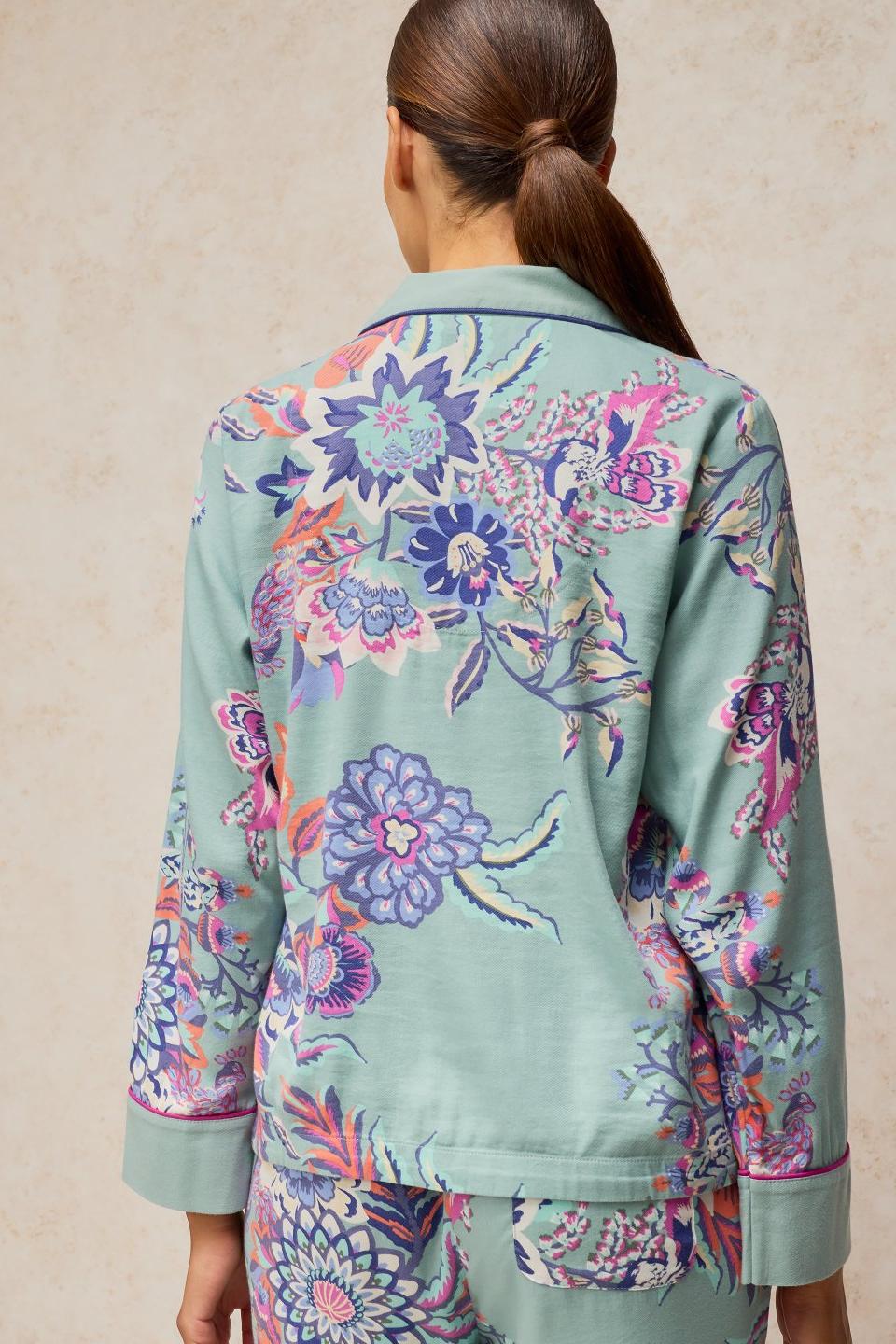 Rear view of a woman wearing a blue floral print organic cotton pyjama top with a button-up collar.