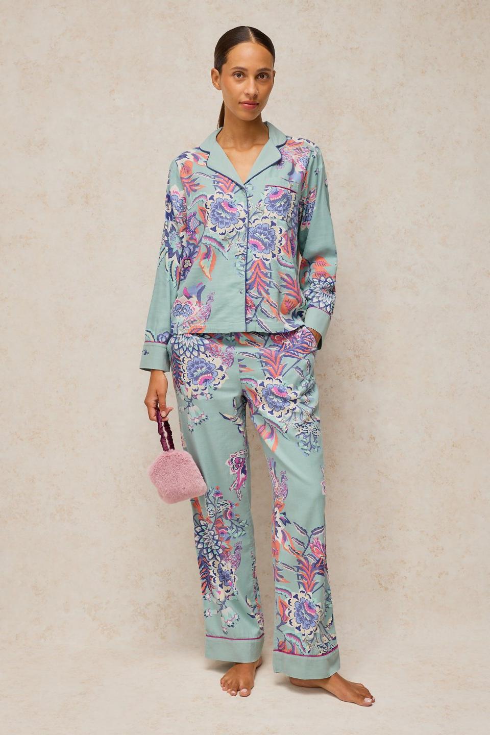 Woman standing wearing a floral organic cotton pyjama top and matching trousers in a light blue print