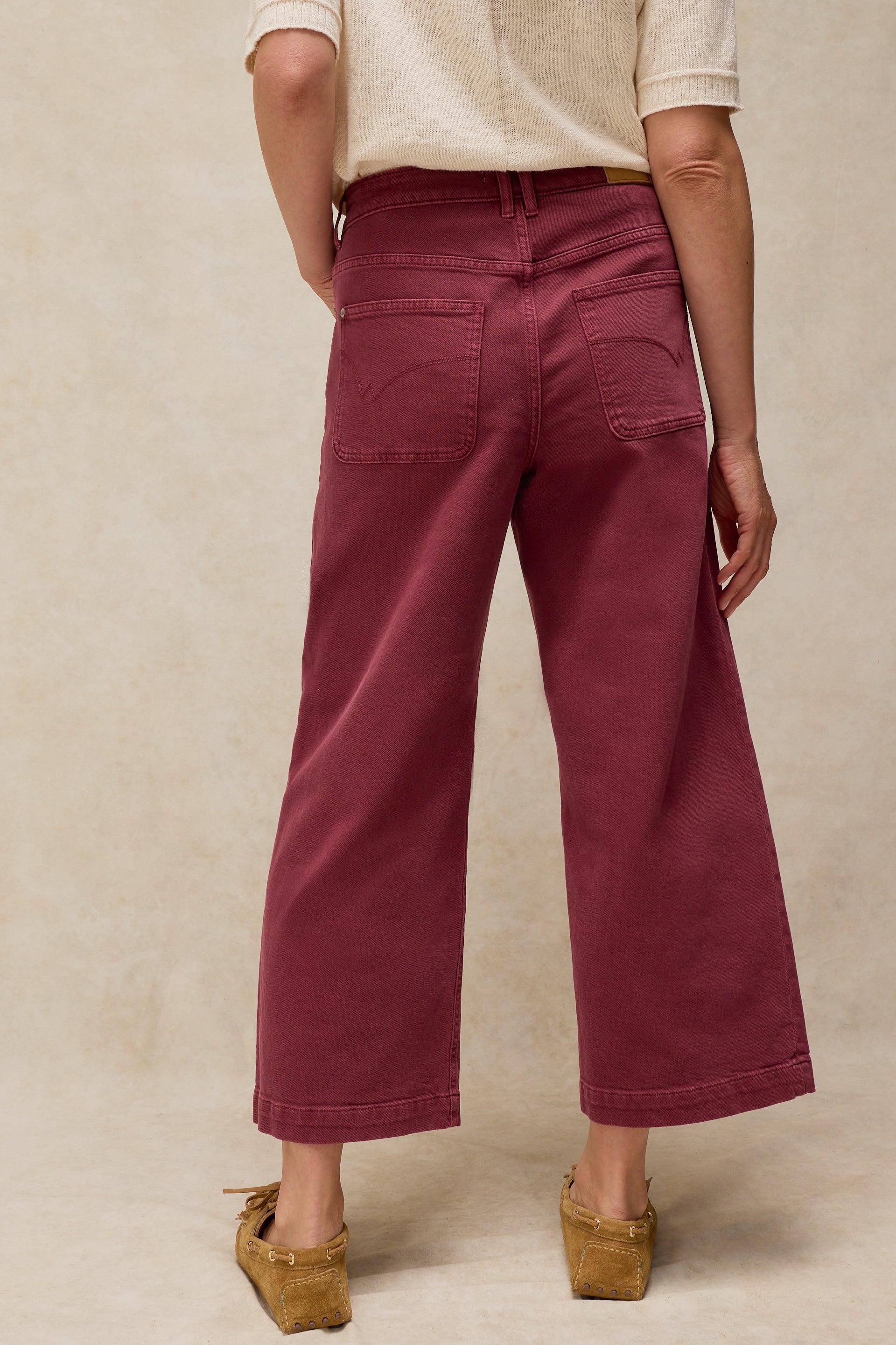 Rear view of a woman wearing burgundy wide-leg organic cotton jeans and a white shirt against a neutral background.