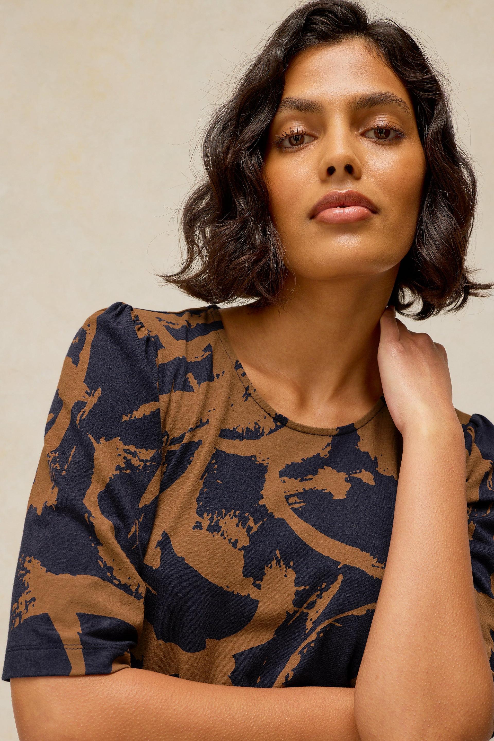 A woman with wavy dark hair wearing a brown and navy organic cotton top against a neutral background.