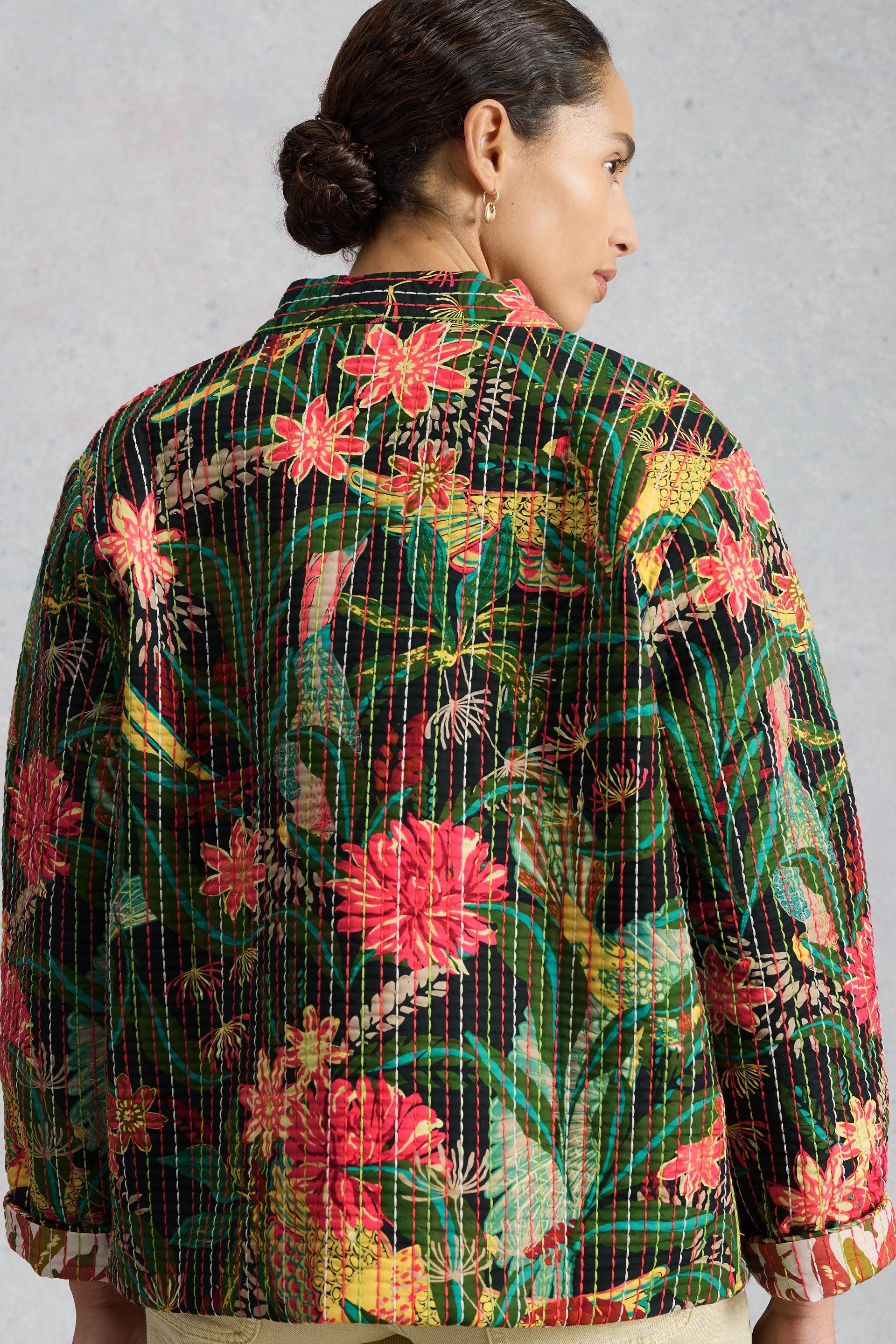 A woman wears a colourful, floral-patterned organic cotton quilted jacket with visible hand-stitched detailing.