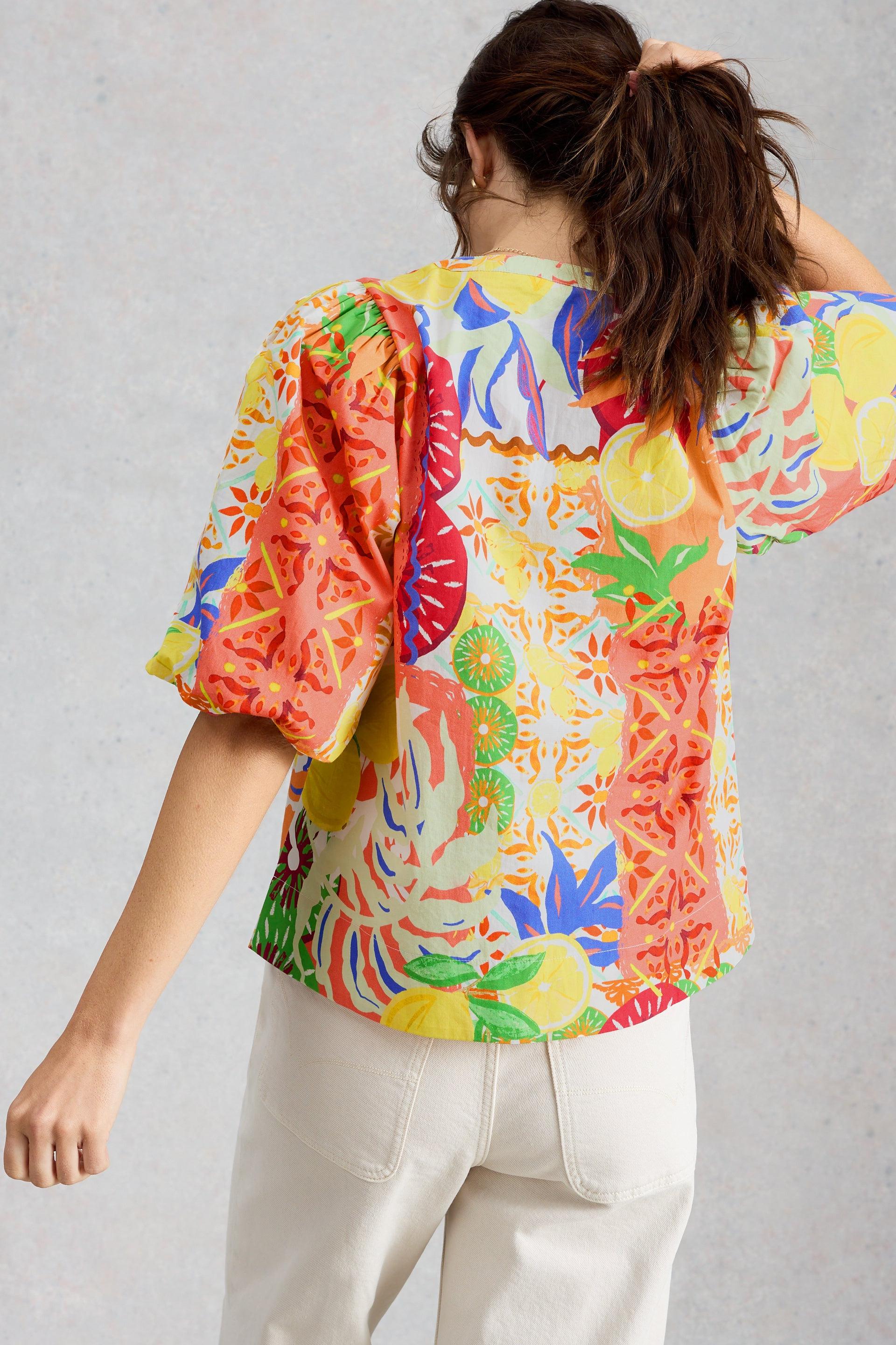 Woman seen from behind wearing a colourful fruit-print organic cotton top with puff sleeves
