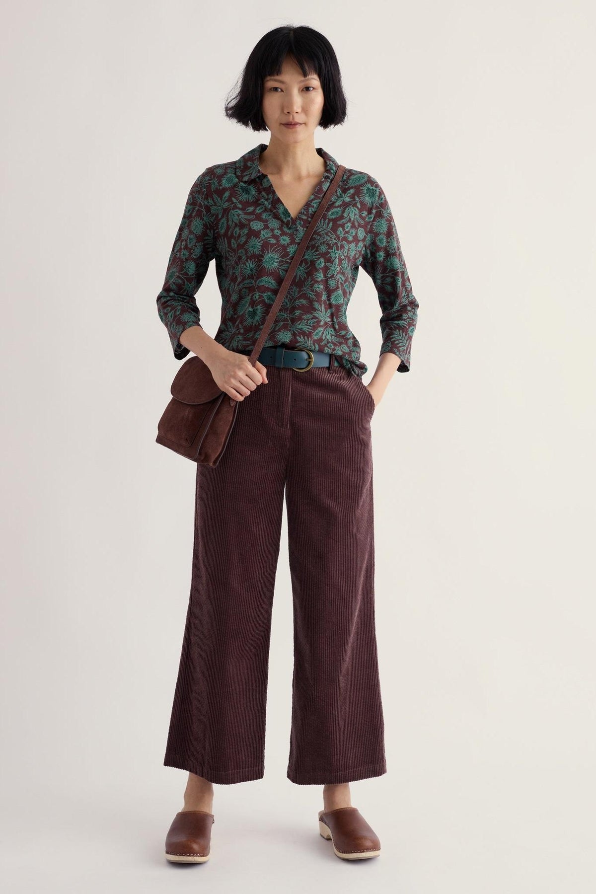 A woman posing in a patterned organic cotton long sleeve shirt and brown corduroy trousers.