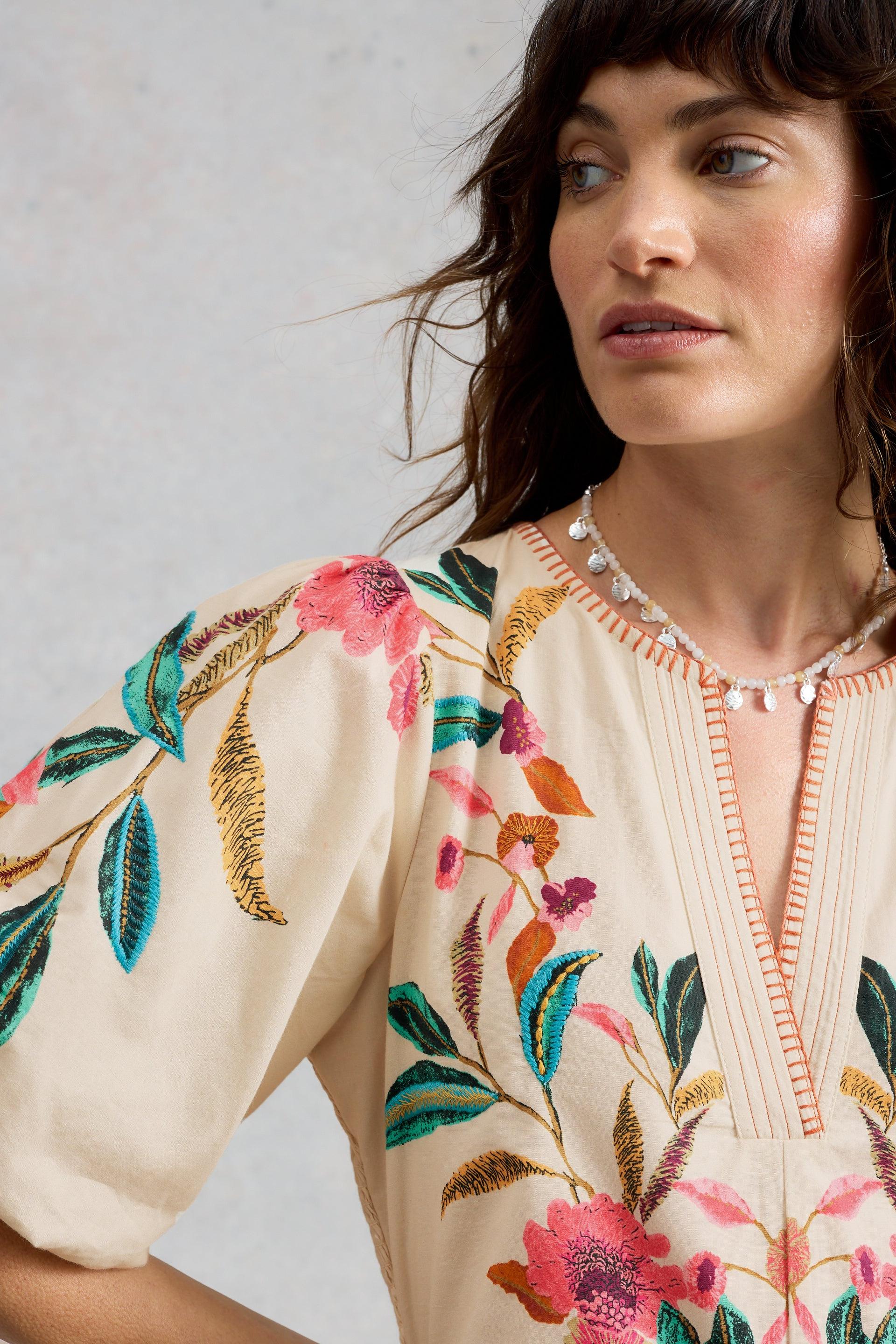 Woman wearing an organic cotton occasion dress with floral embroidery by White Stuff.