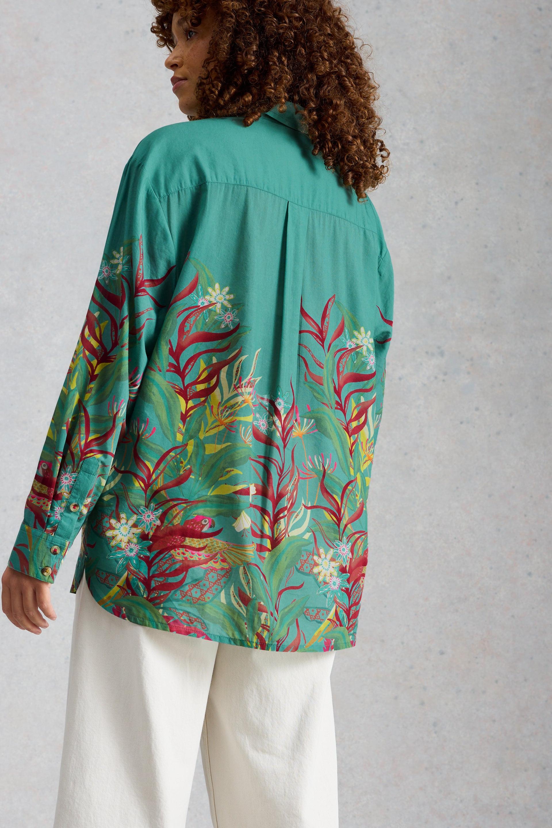 A woman from behind wearing a green organic cotton printed shirt with floral and bird patterns from White Stuff.