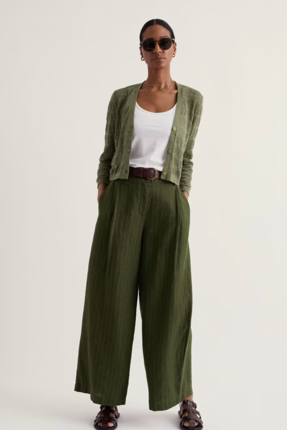Woman wearing an organic cotton green cardigan, white tank top, and wide-leg trousers from Seasalt