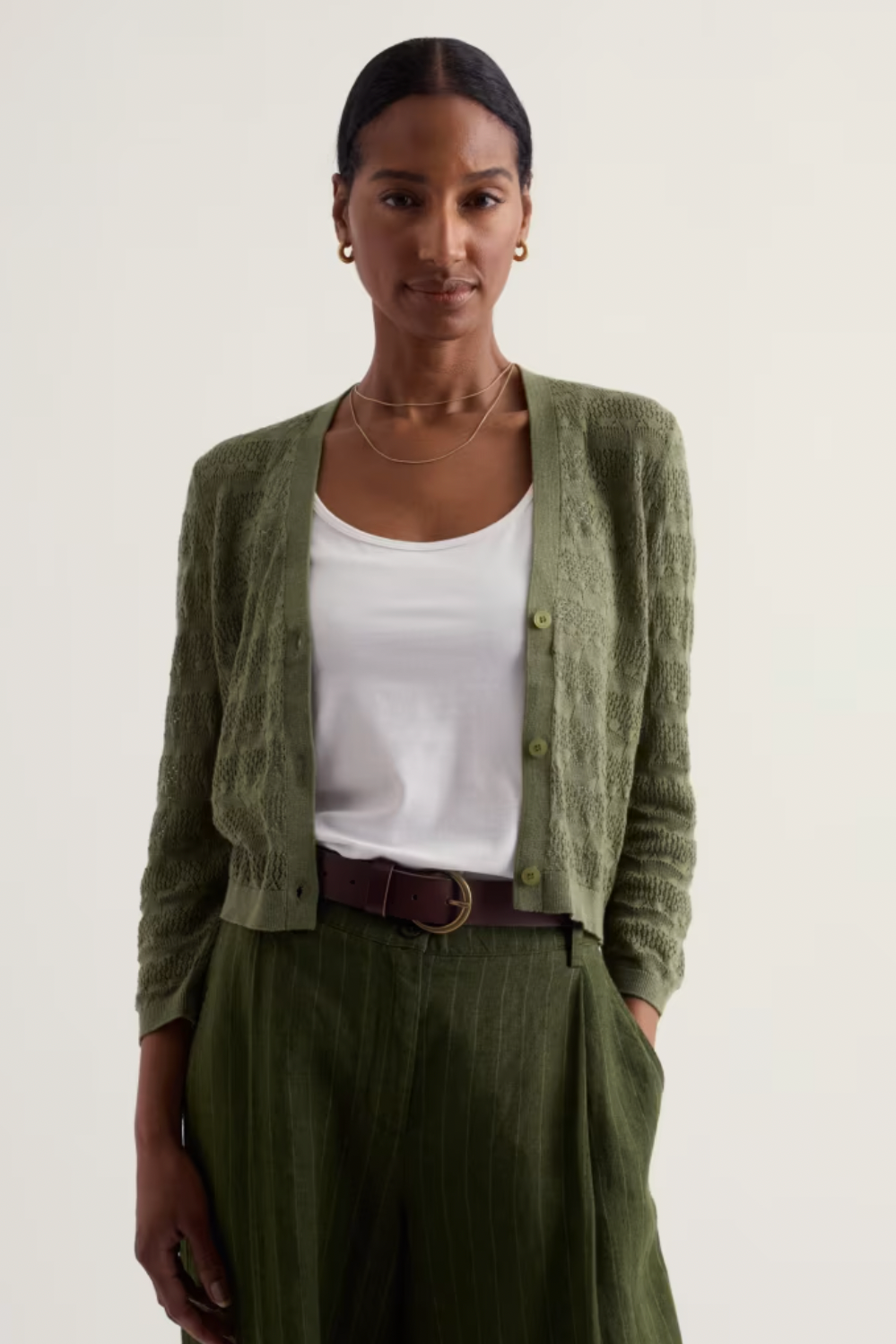A woman posing in a textured olive green organic cotton cardigan by Seasalt.