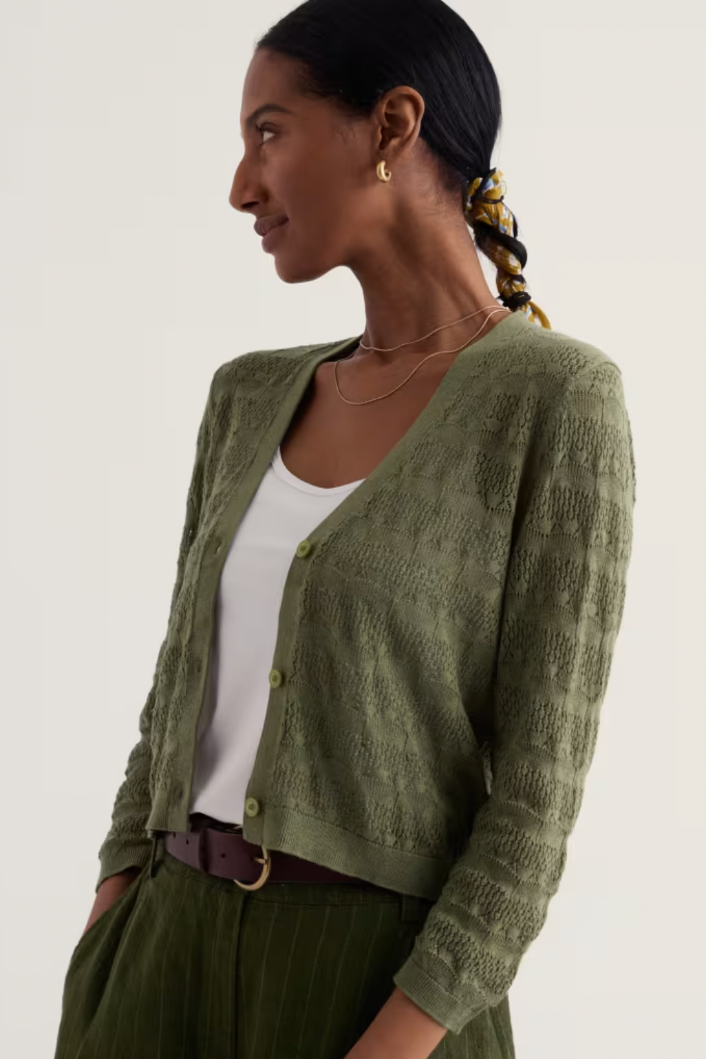 A woman wearing a textured green organic cotton cardigan over a white top.