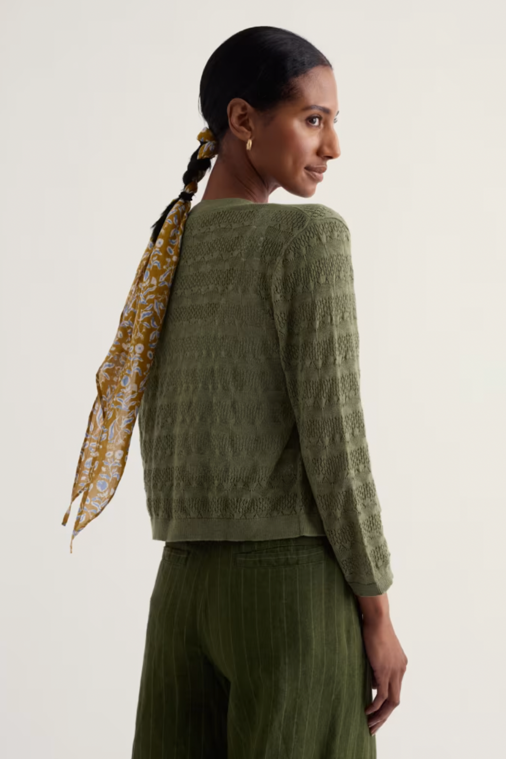 A woman wearing a textured organic cotton green Seasalt cardigan with a patterned hair scarf.