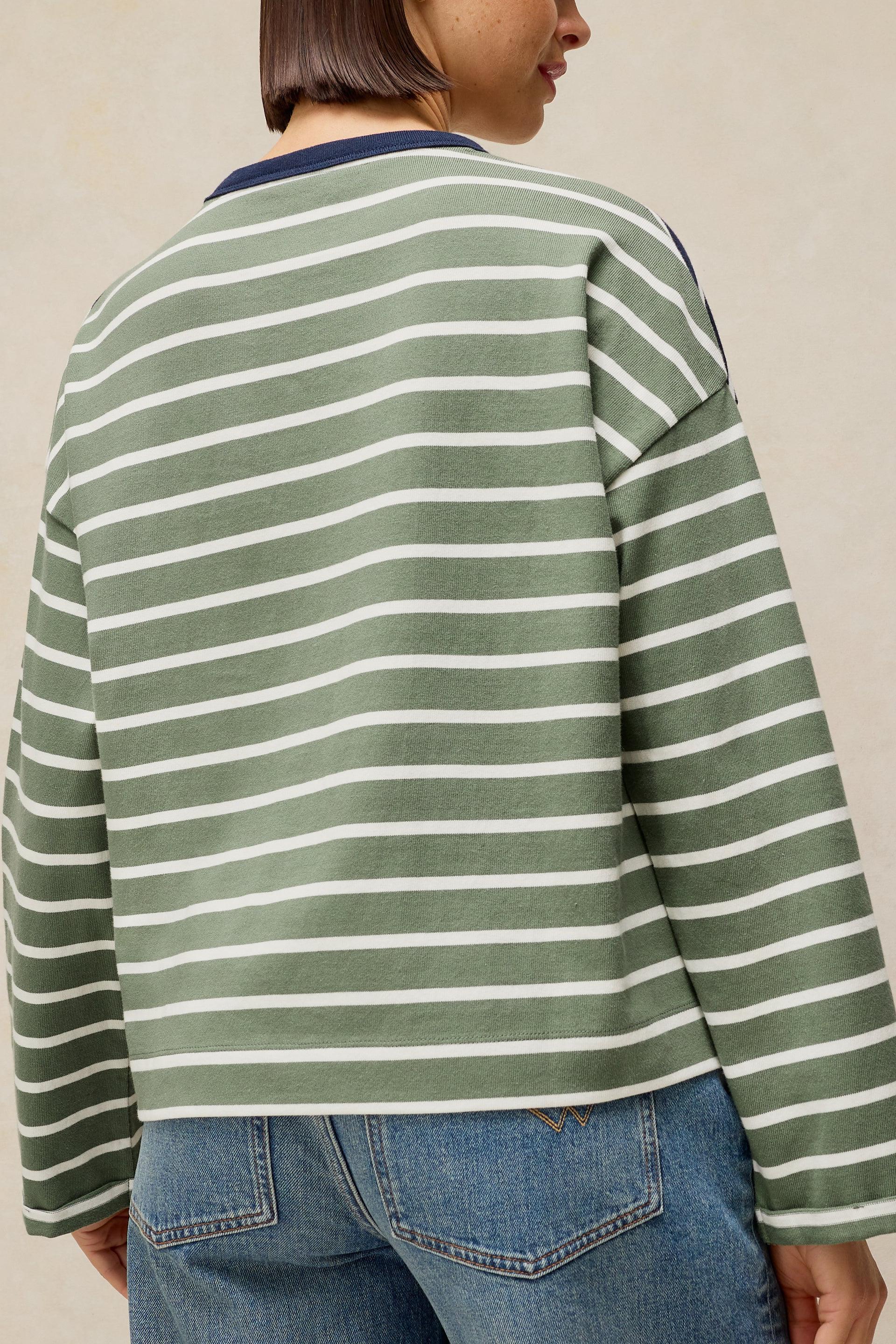 A person shown from the back wearing a green and white horizontally striped long-sleeve top with blue jeans, against a plain beige background.