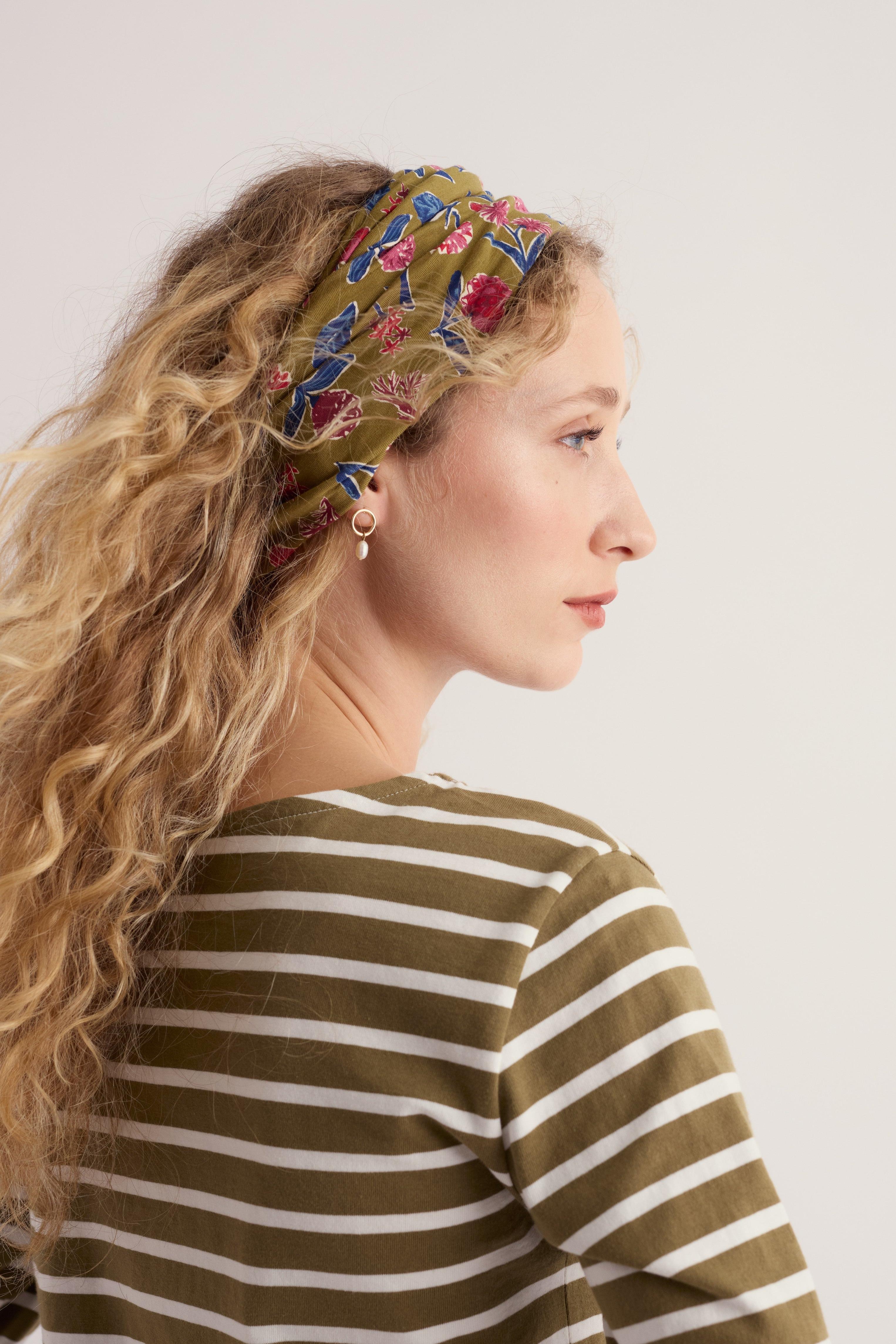 Profile view of a woman with curly blonde hair wearing a floral headband and an organic cotton striped shirt
