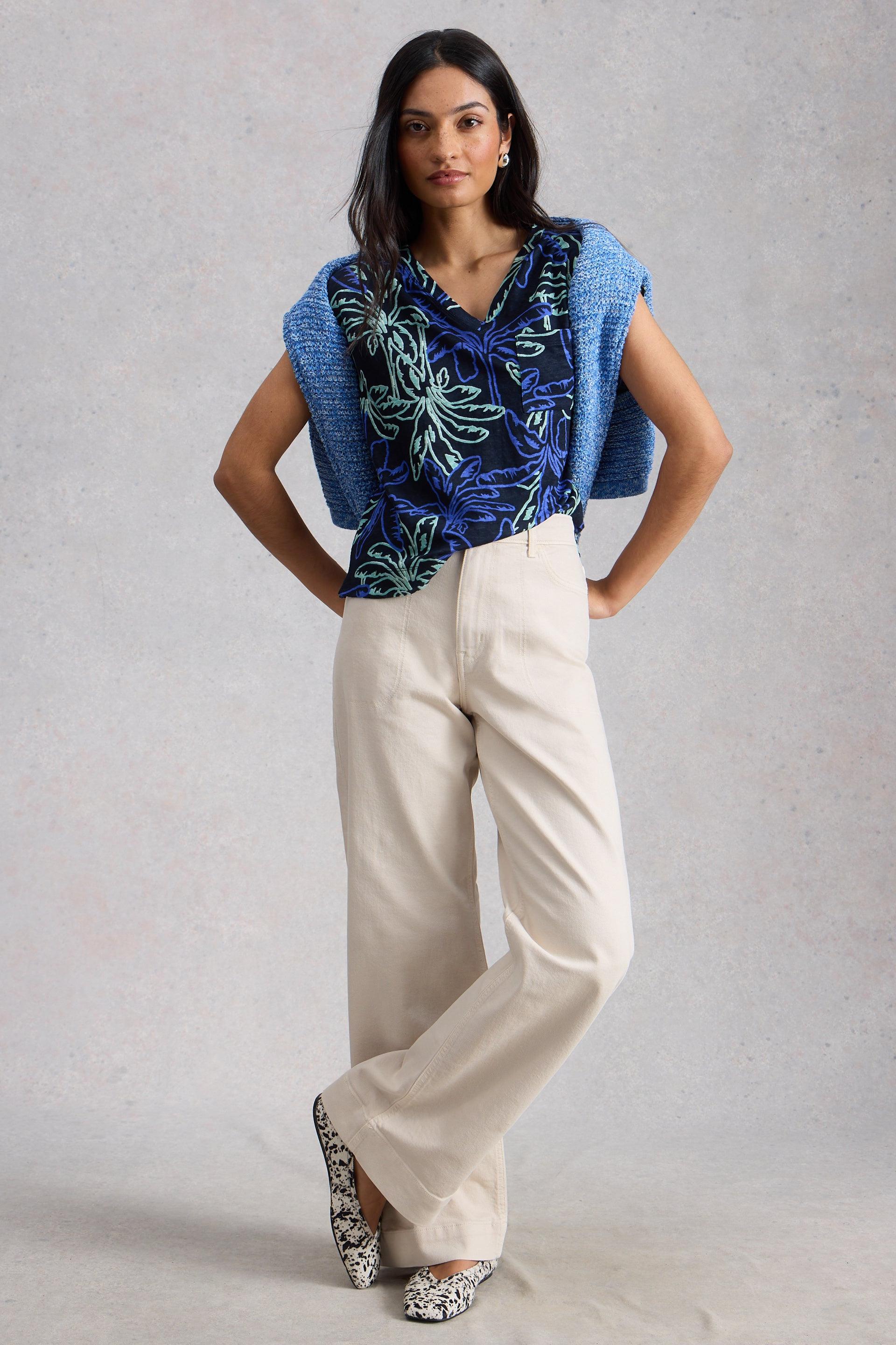 Woman wearing a blue patterned top and beige organic cotton jeans against a gray background