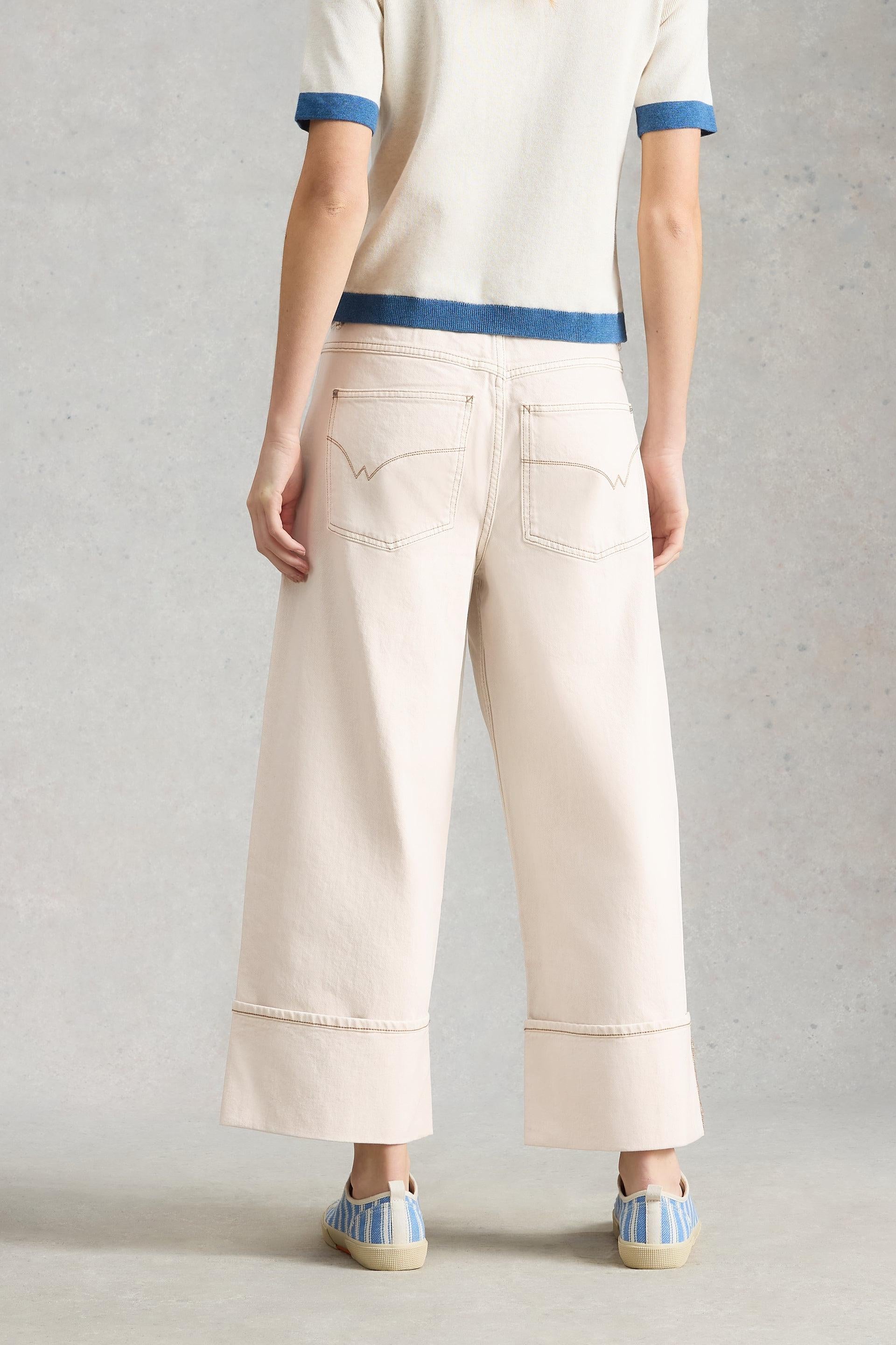 Rear view of a person wearing beige wide-leg trousers and a white top against a neutral background.
