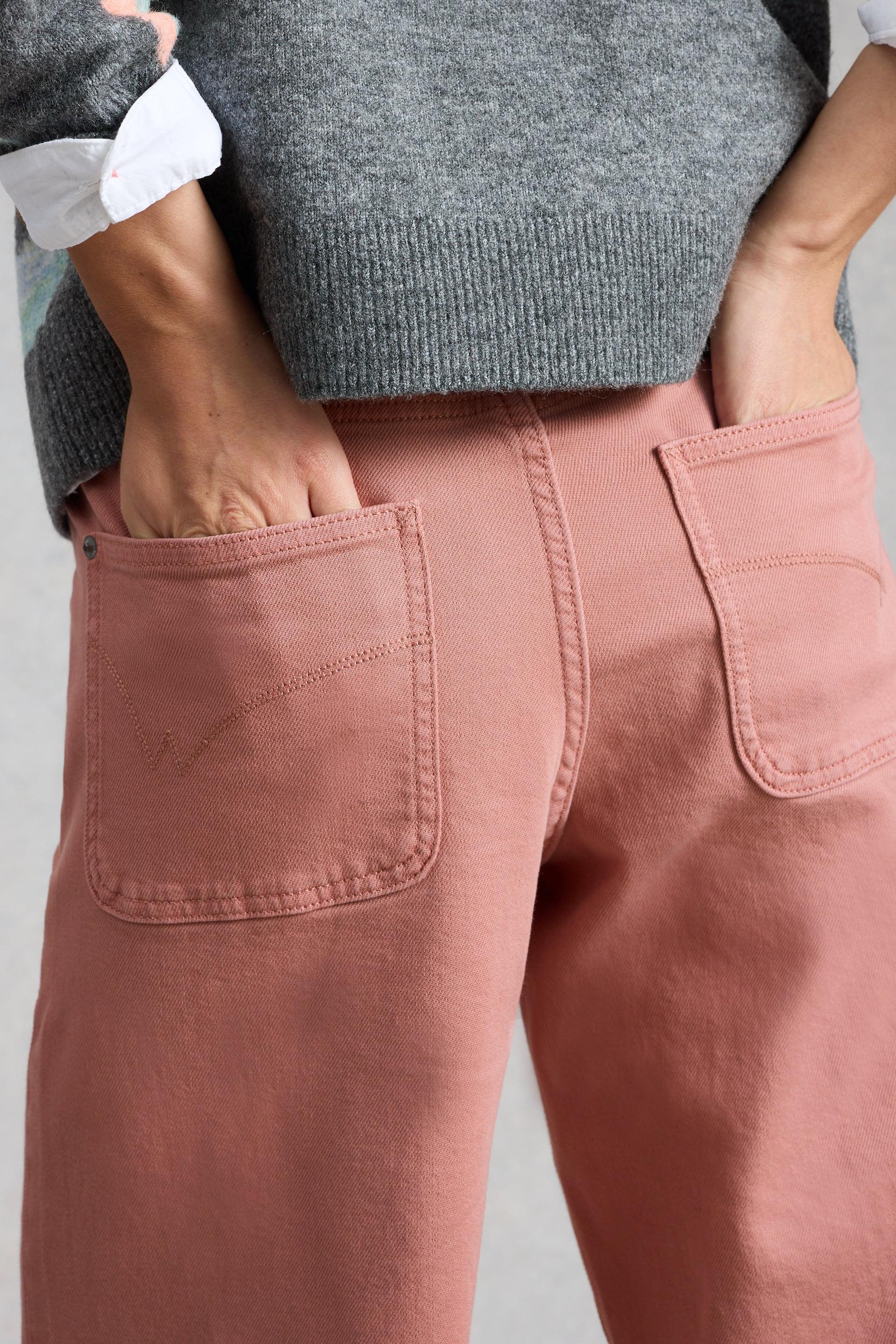 A person with hands in the back pockets of dusty pink organic cotton trousers from White Stuff.