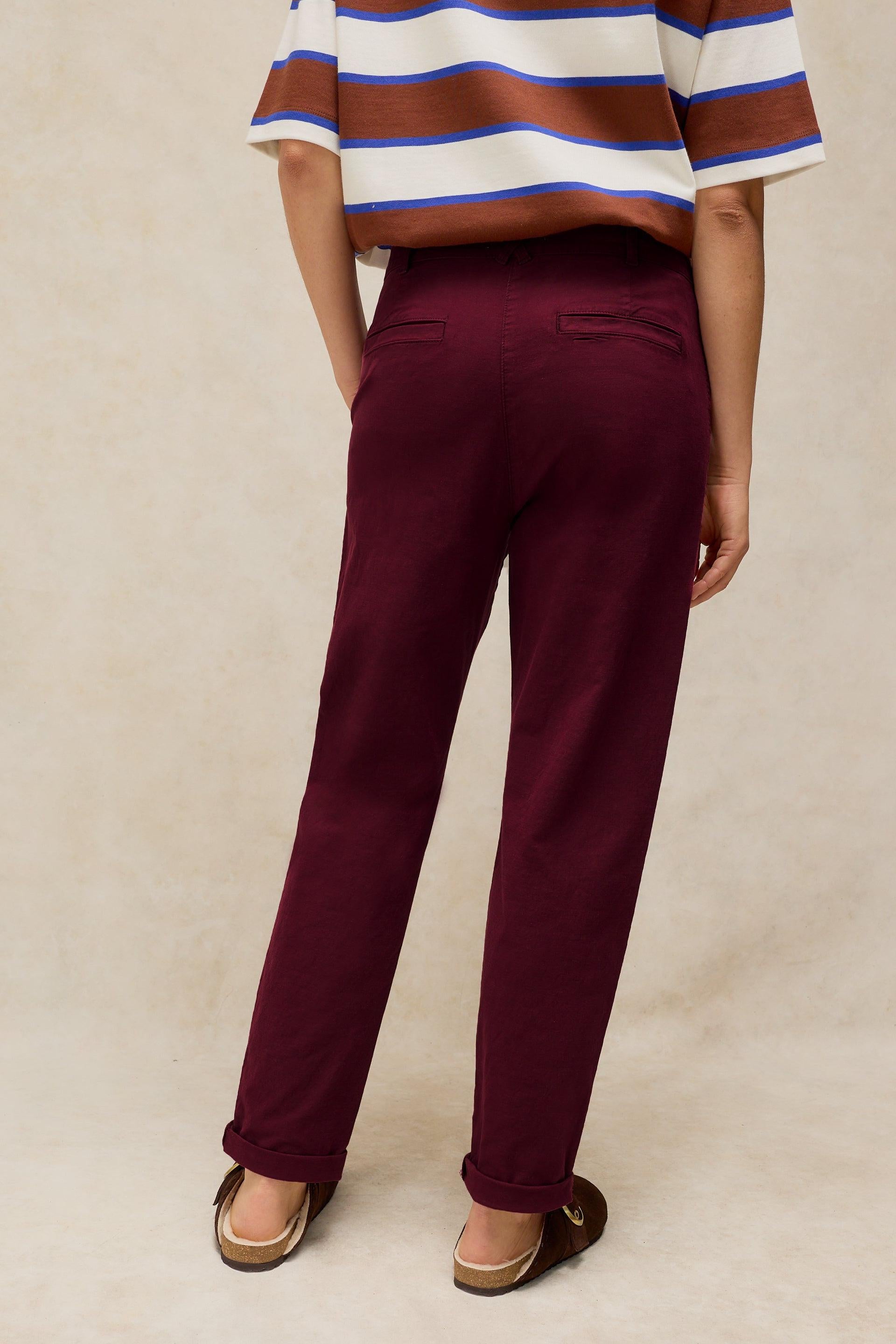 A person standing with their back to the camera wearing burgundy organic cotton trousers and a striped shirt.