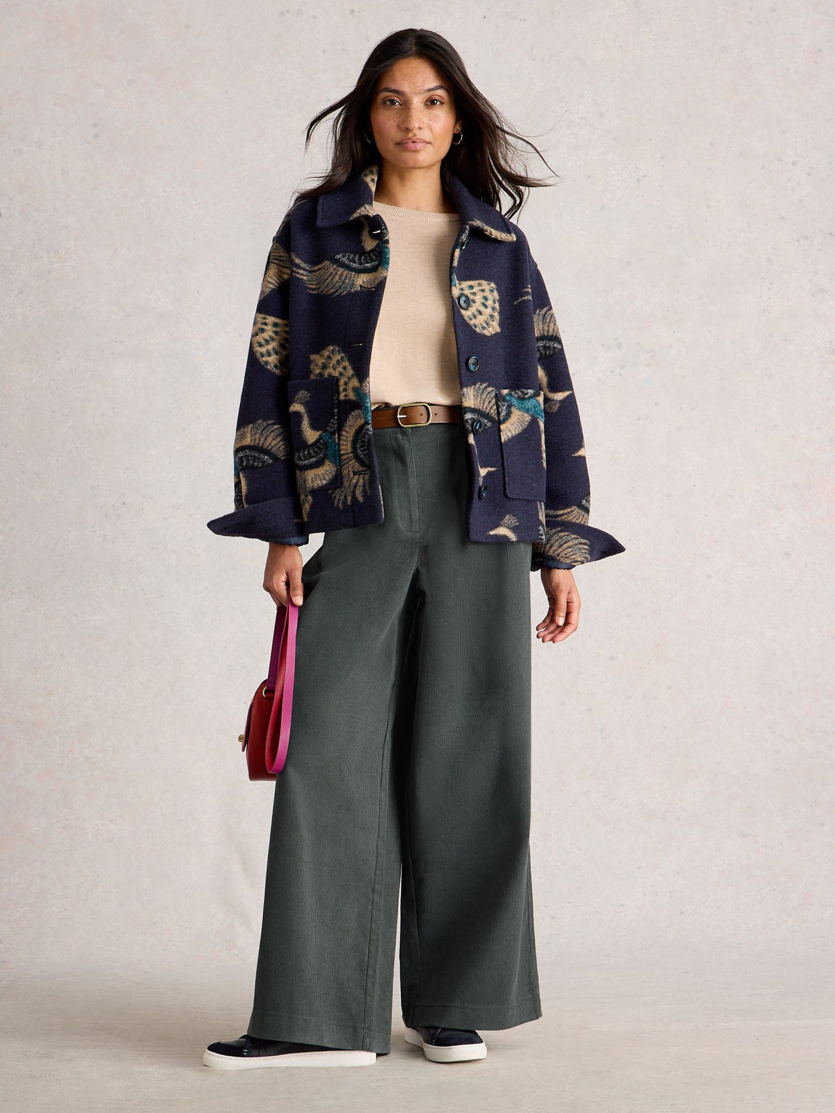 A woman modeling a dark patterned jacket and dark wide leg cords against a neutral background.