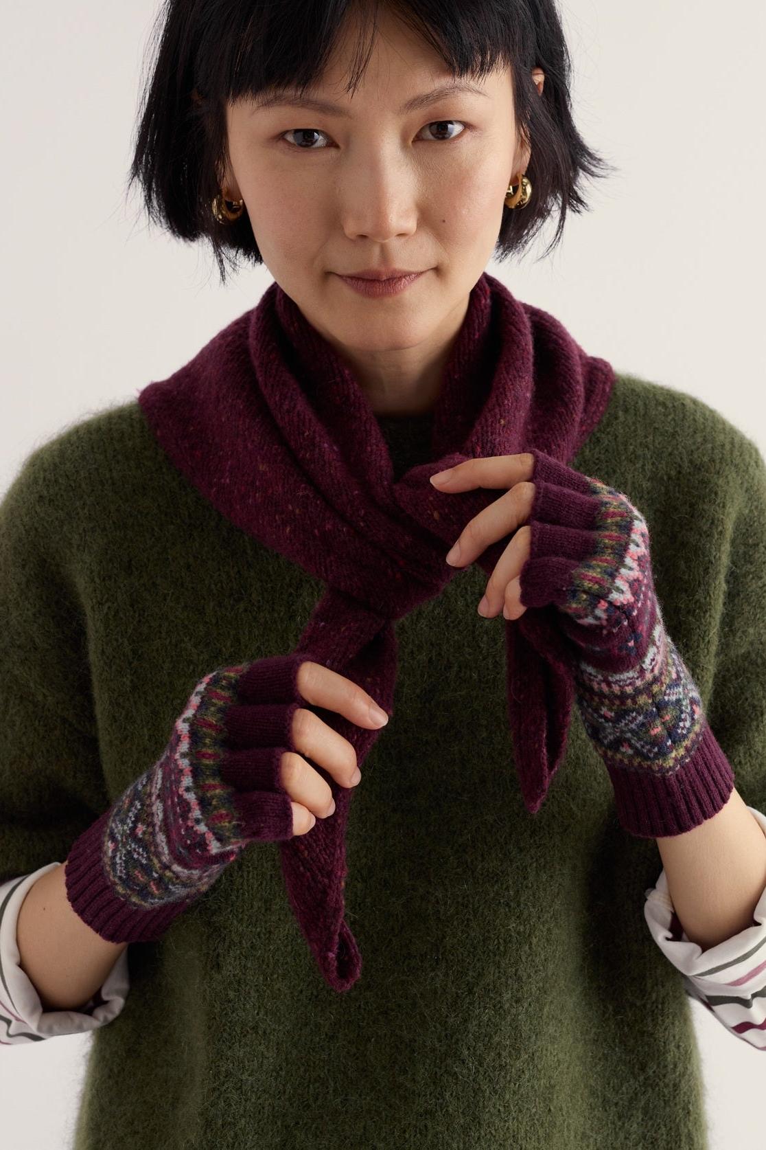 A woman wearing patterned, purple wool fingerless Seasalt knit gloves and a coordinating scarf.