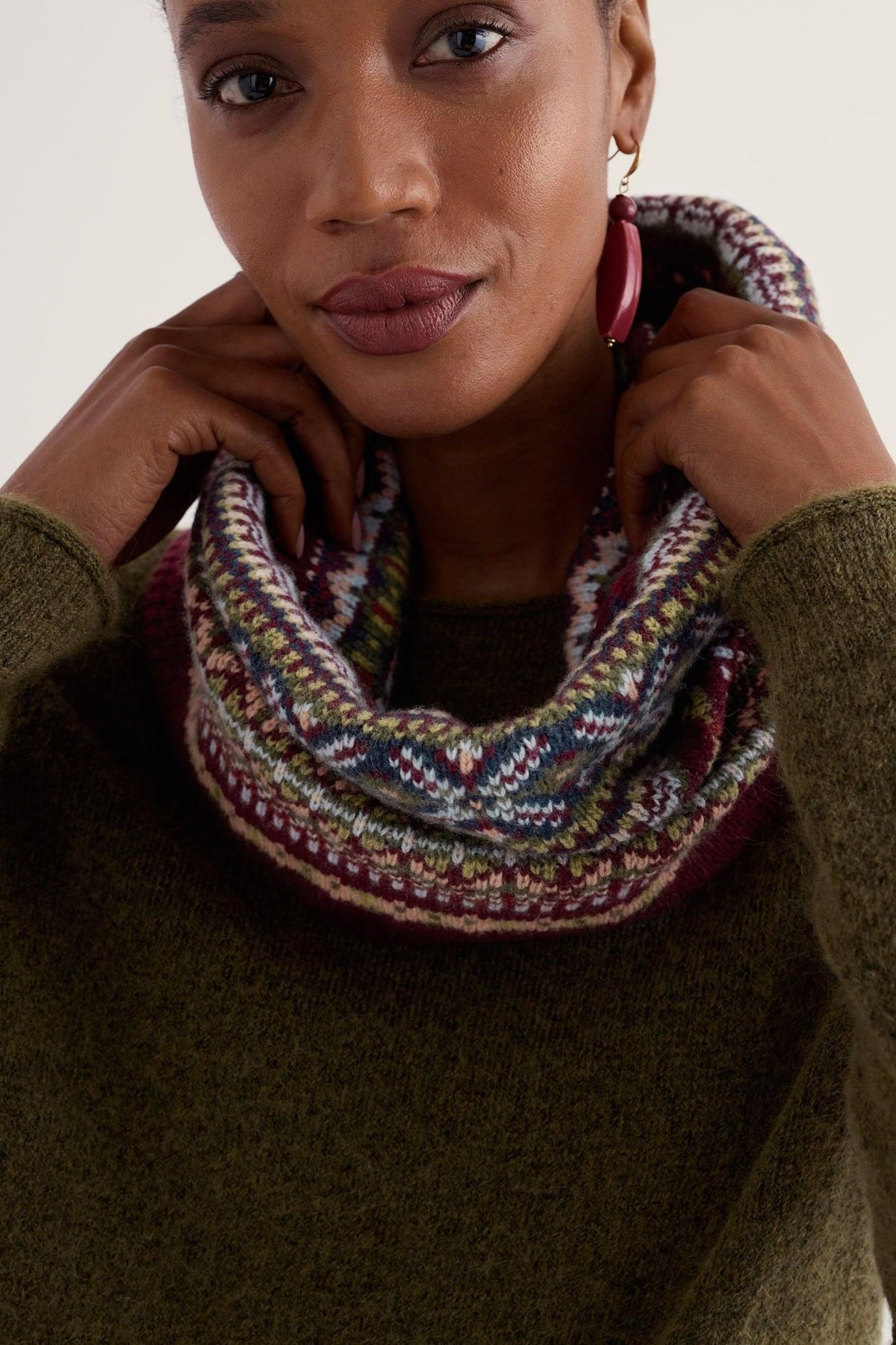 A woman wearing a decorative patterned wool snood scarf over a green sweater.