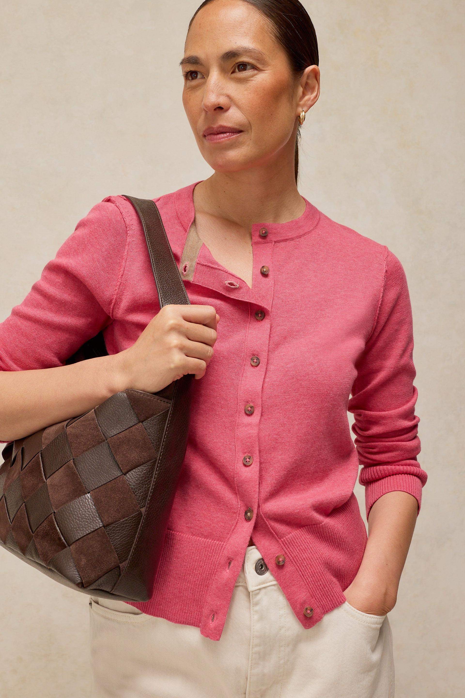 Woman wearing a bright pink button-down cardigan and carrying a brown woven leather handbag