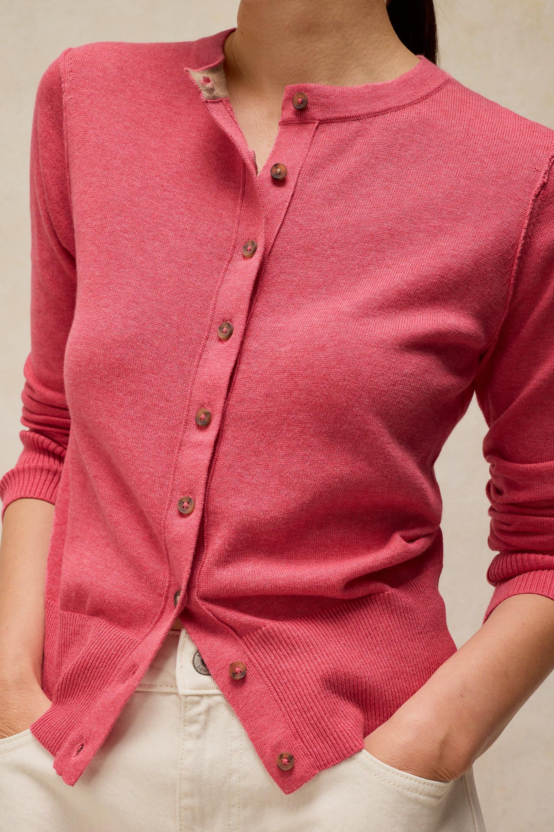 Woman wearing a bright pink button-down cardigan and white organic cotton pants with hands in pockets