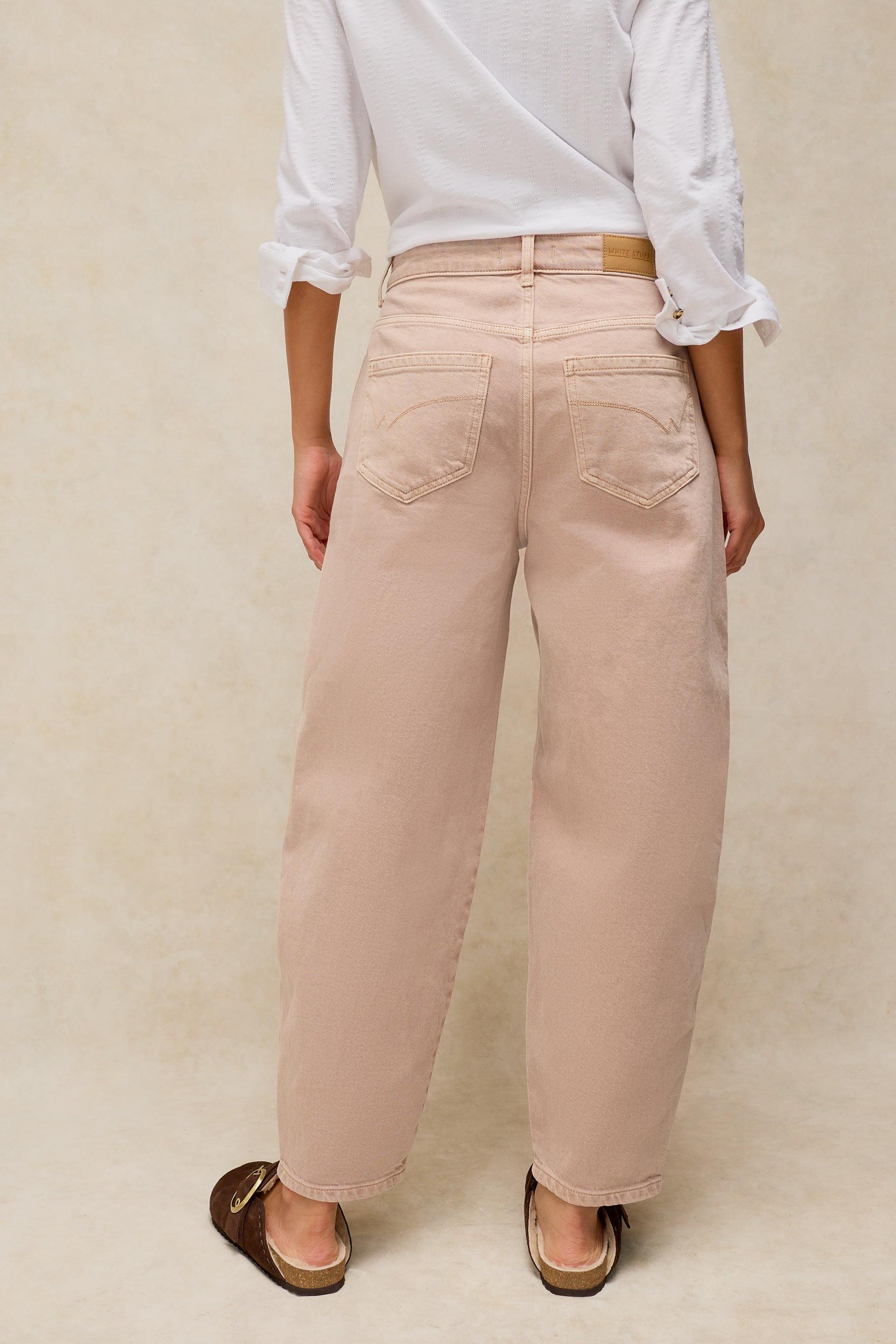 Rear view of a person wearing beige organic cotton jeans and a white shirt against a neutral background.