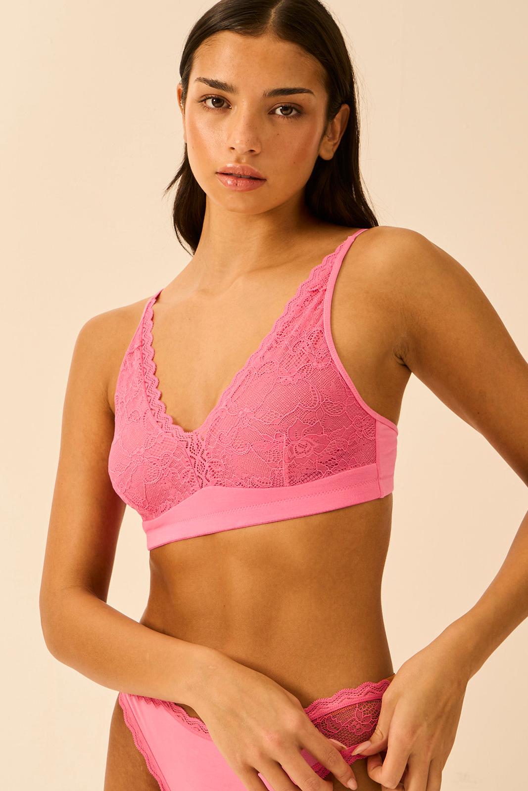 A woman wearing a vibrant pink lace bralette from Stripe & Stare, posing against a neutral studio background