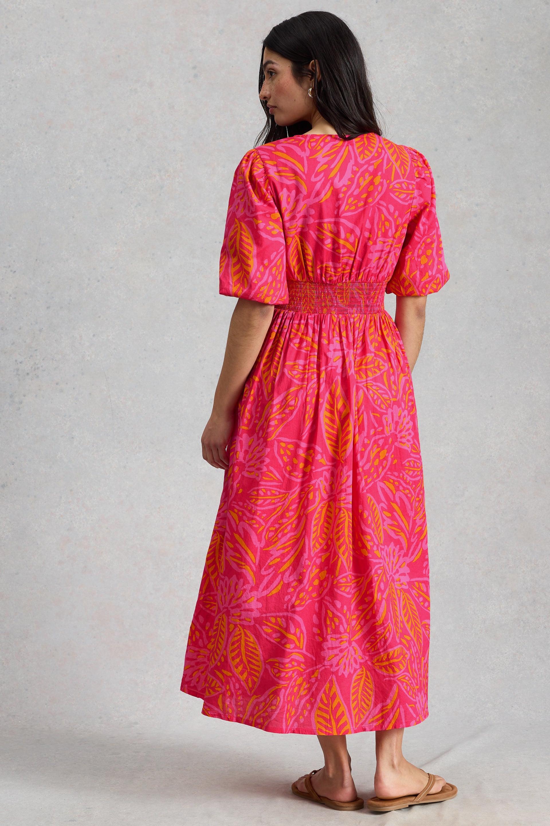 A woman from behind wearing a pink and orange leaf-print organic cotton midi dress with puff sleeves.