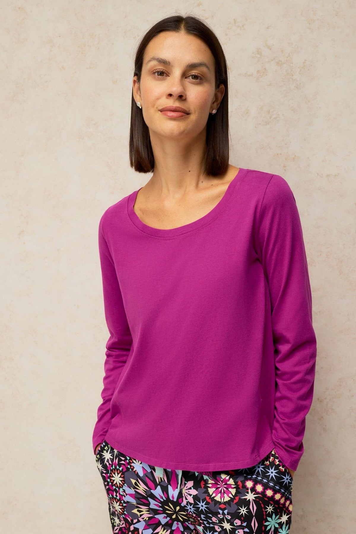 A woman posing in a vibrant pink long-sleeve organic cotton pyjama top.