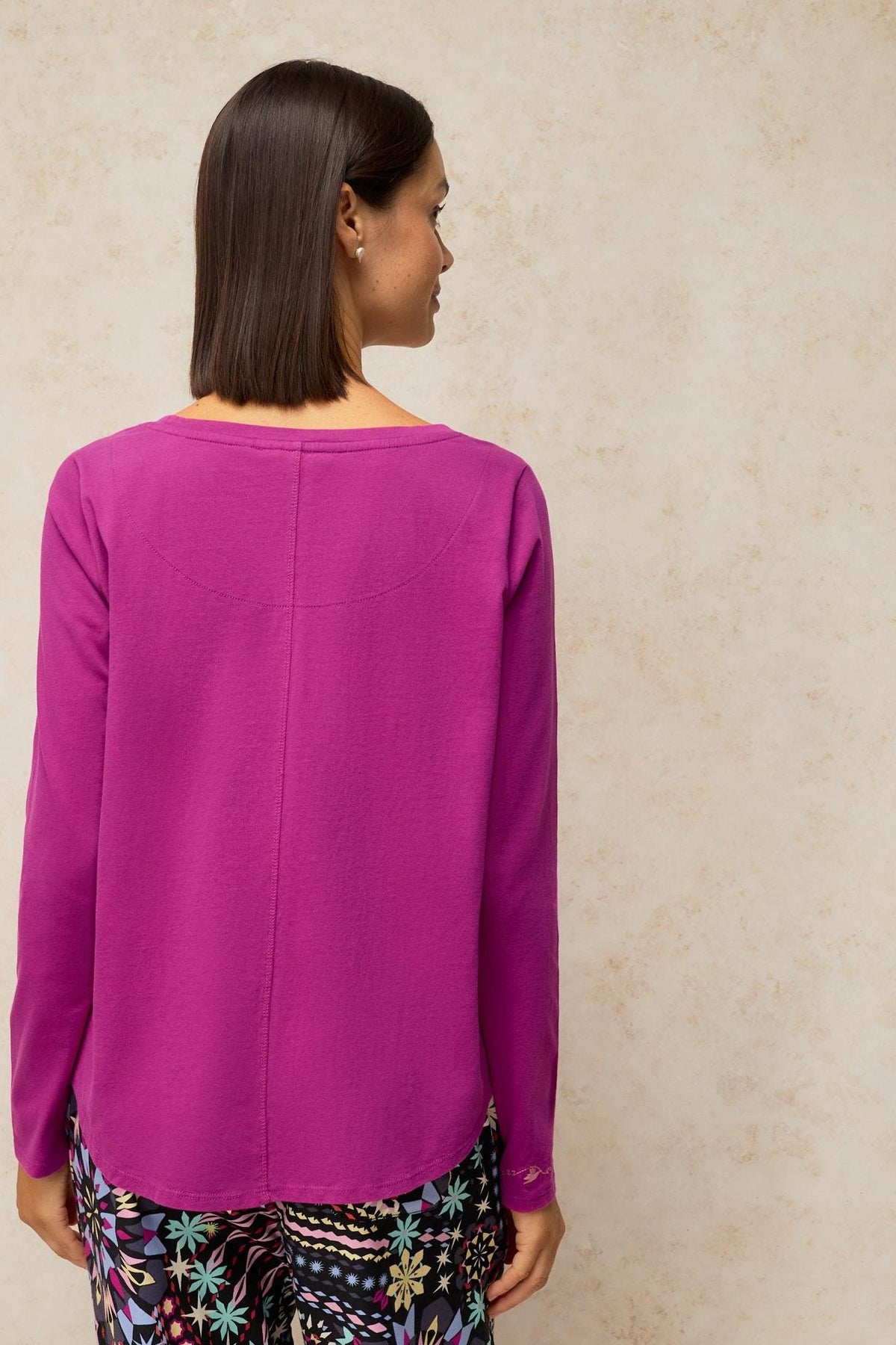 Woman standing with her back to the camera wearing a pink organic cotton pyjama top
