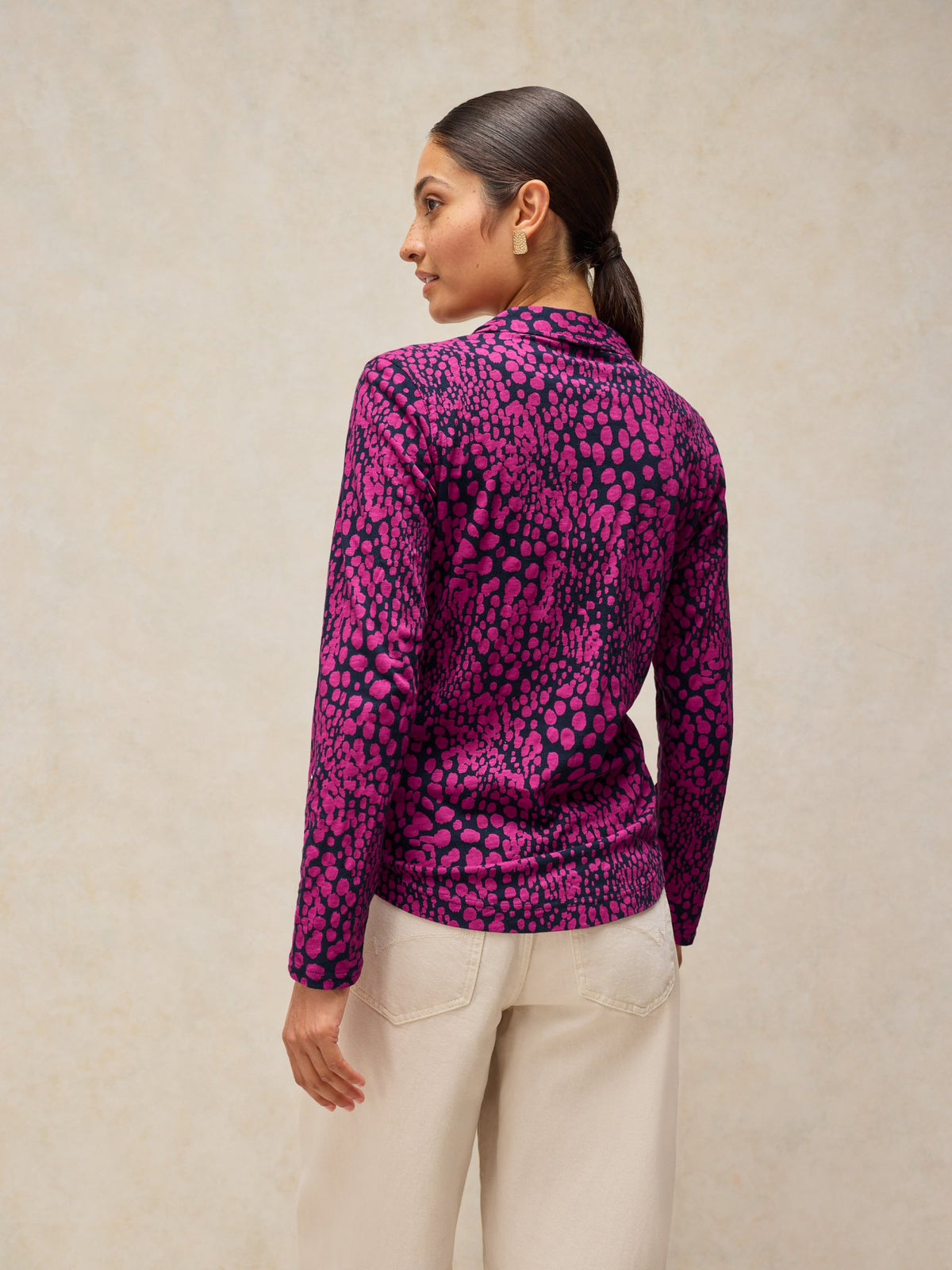 A woman wearing a long-sleeved pink and black printed cotton jersey blouse with casual white pants.
