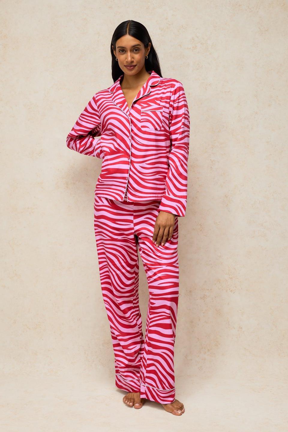 A woman wearing a pink zebra print organic cotton pyjama set standing against a neutral background.