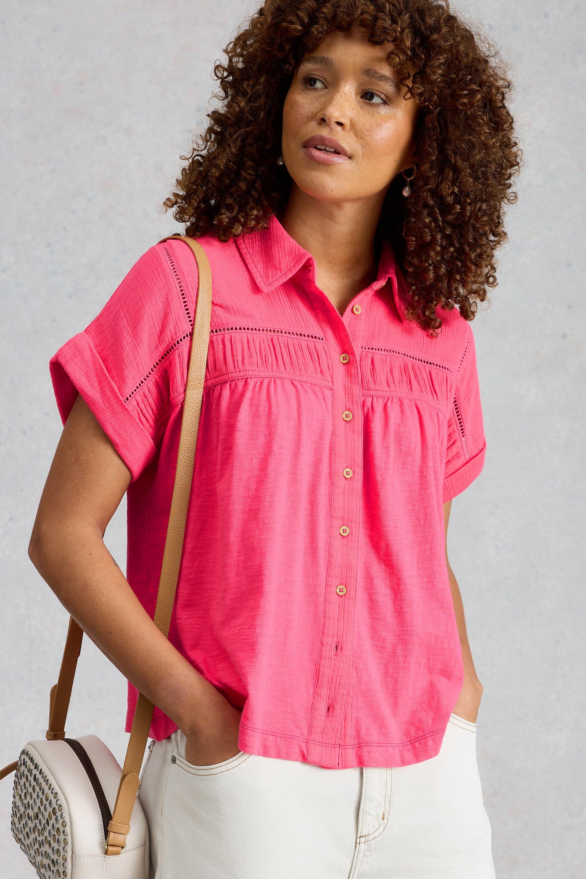 Woman wearing a bright pink organic cotton button-up shirt by White Stuff with a crossbody bag.