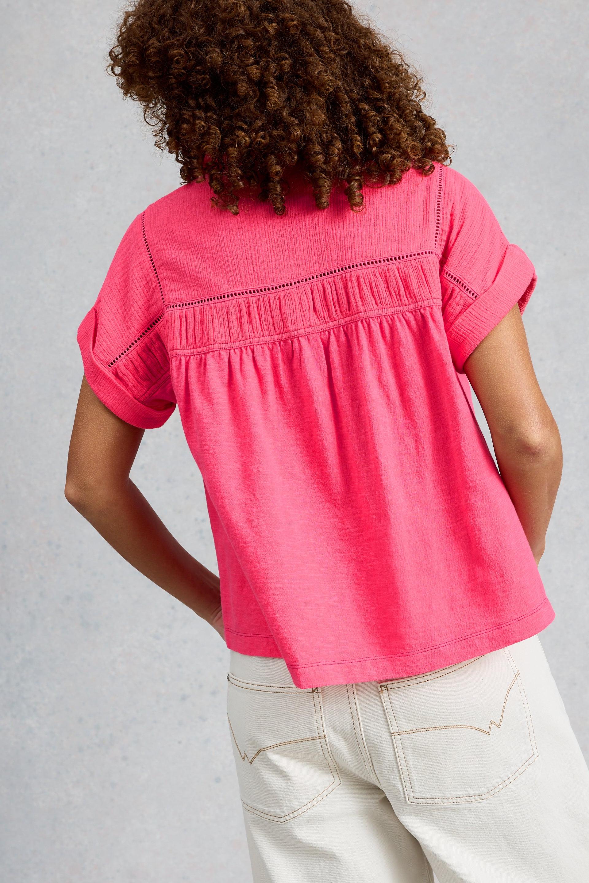 Woman wearing a bright pink White Stuff organic cotton top with short sleeves and textured fabric.