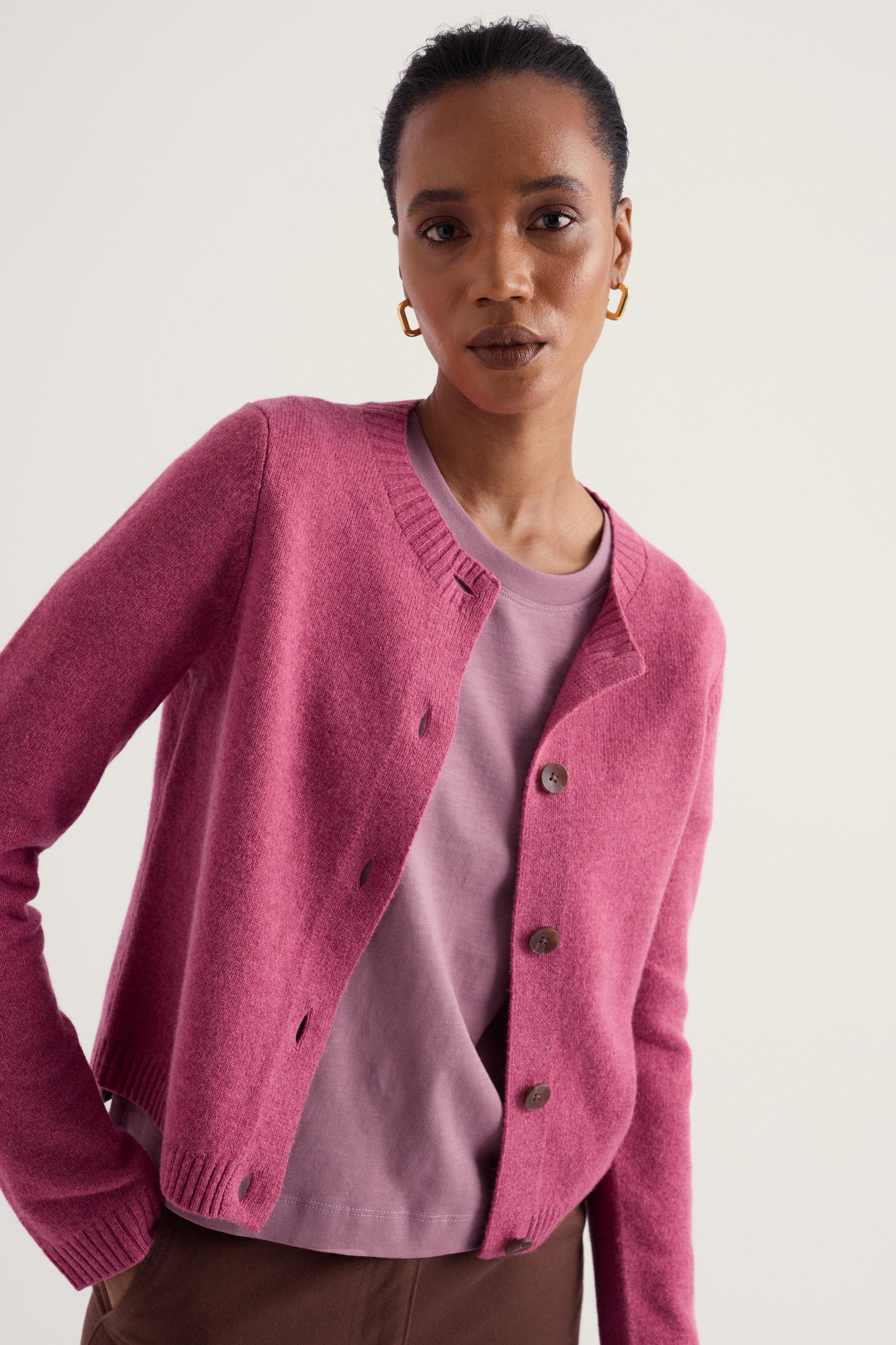A woman wearing a pink wool knit cardigan over a dusty pink top, photographed against a plain light background.