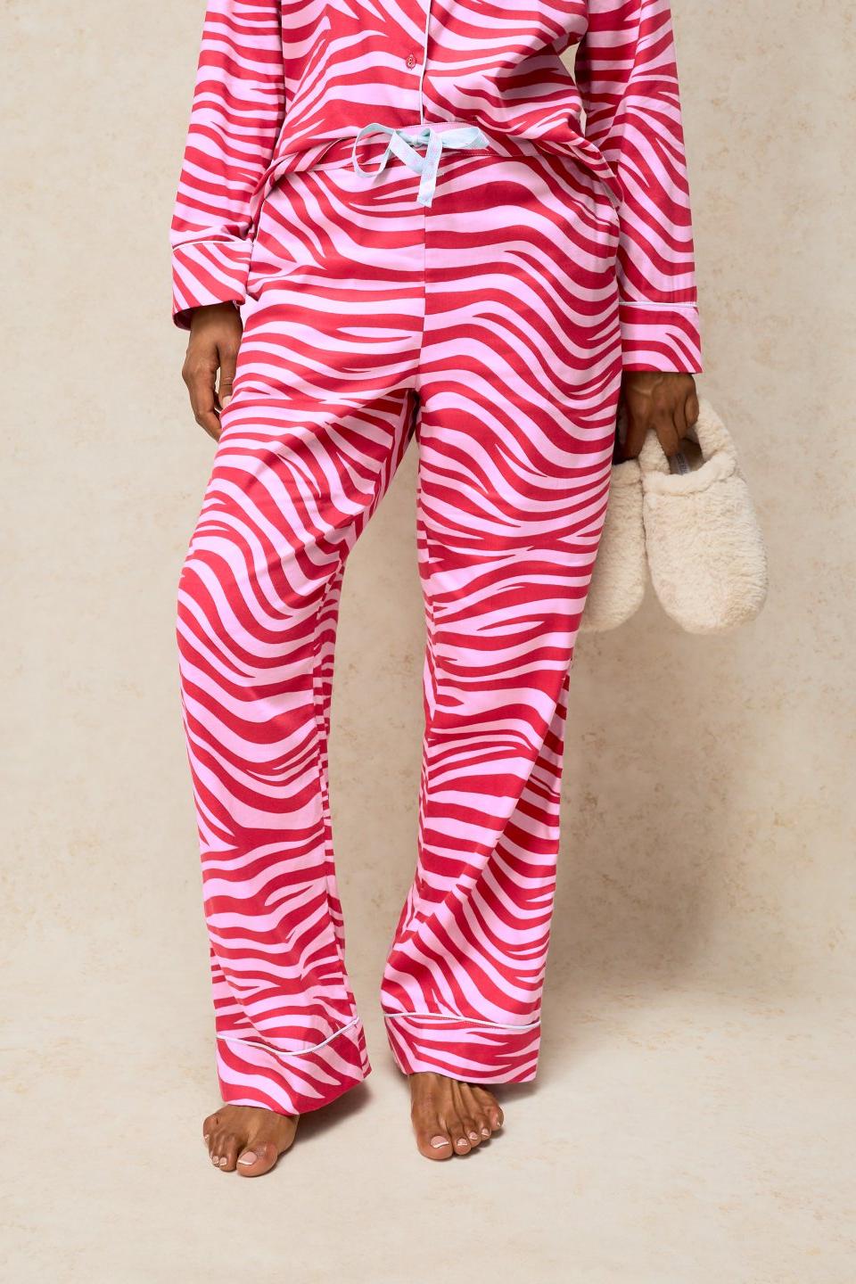 Woman wearing pink zebra print organic cotton pyjama bottoms holding cosy slippers