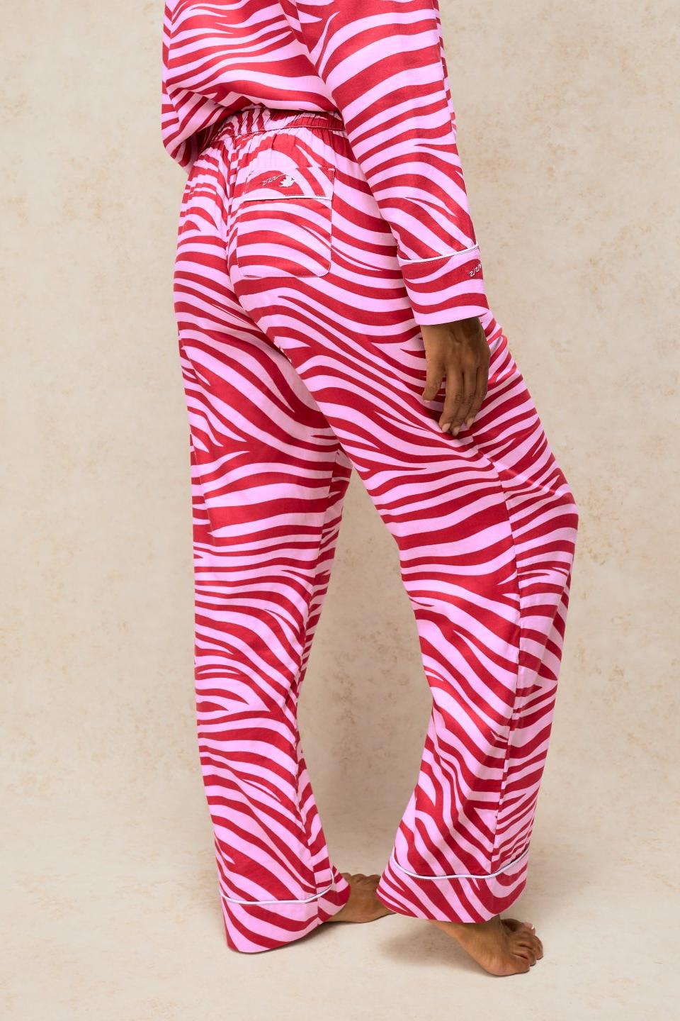 Woman wearing pink zebra print organic cotton pyjama bottoms with matching top against a neutral background.