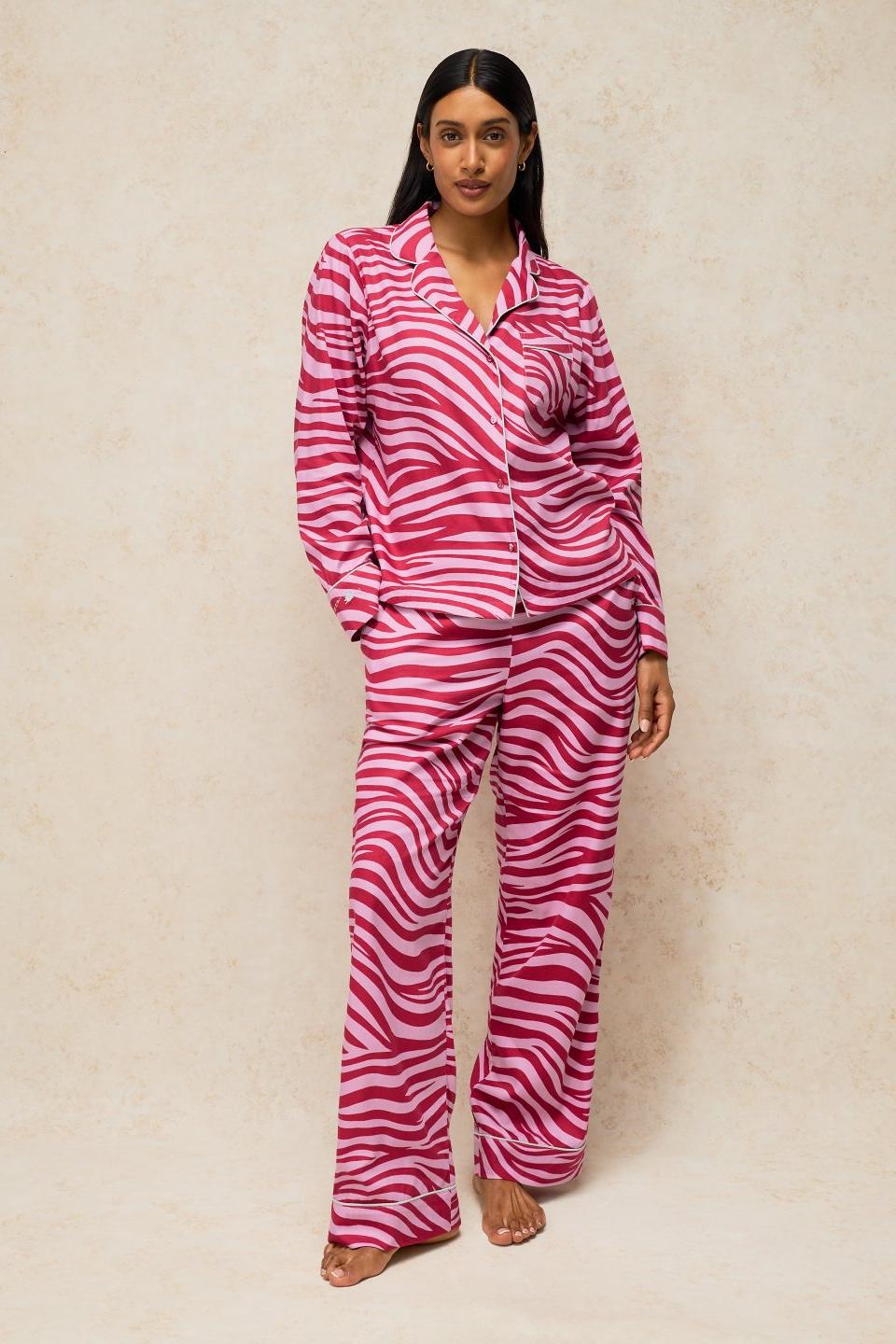 A woman wearing a cosy pink zebra print organic cotton pyjama set with a long-sleeved button-up top and matching trousers.