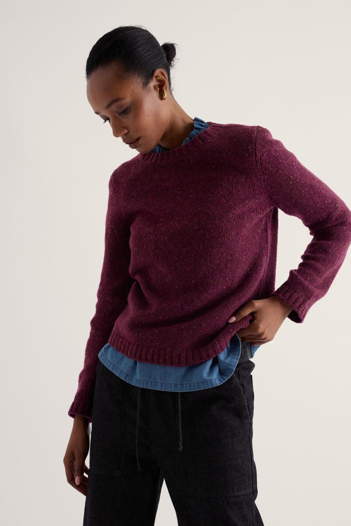 A woman modeling a Seasalt Cornwall plum merino wool jumper over a denim shirt against a plain background.
