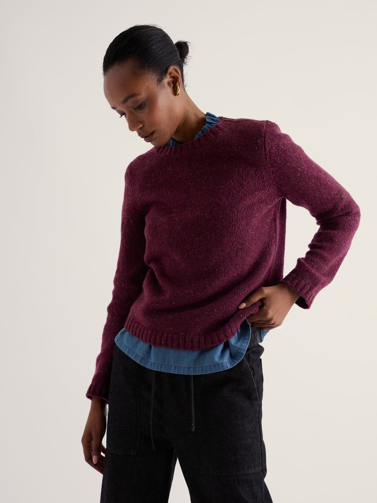 A woman modeling a Seasalt Cornwall plum merino wool jumper over a denim shirt against a plain background.