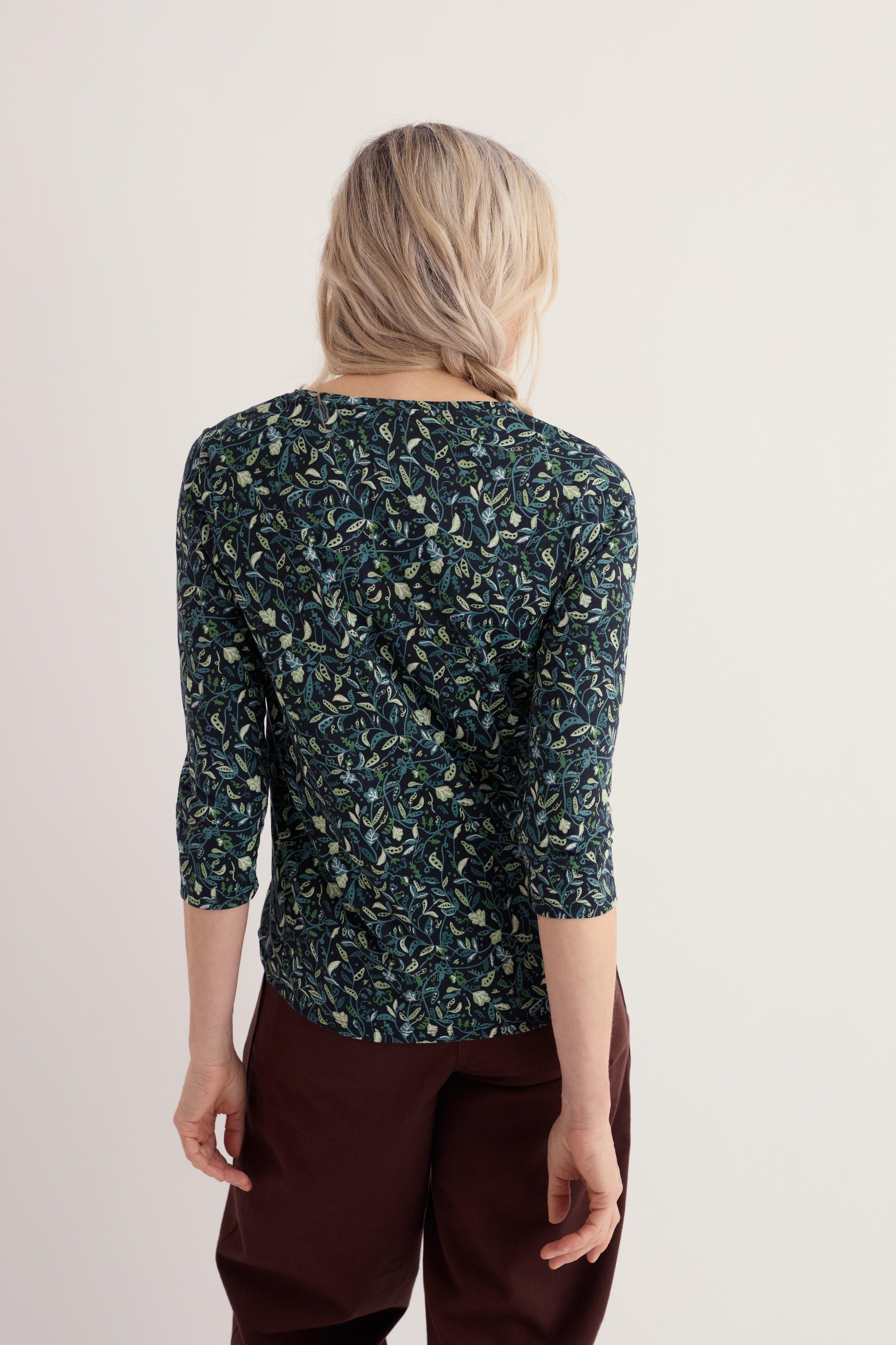 Rear view of a woman wearing a dark floral print organic cotton top against a plain studio background.
