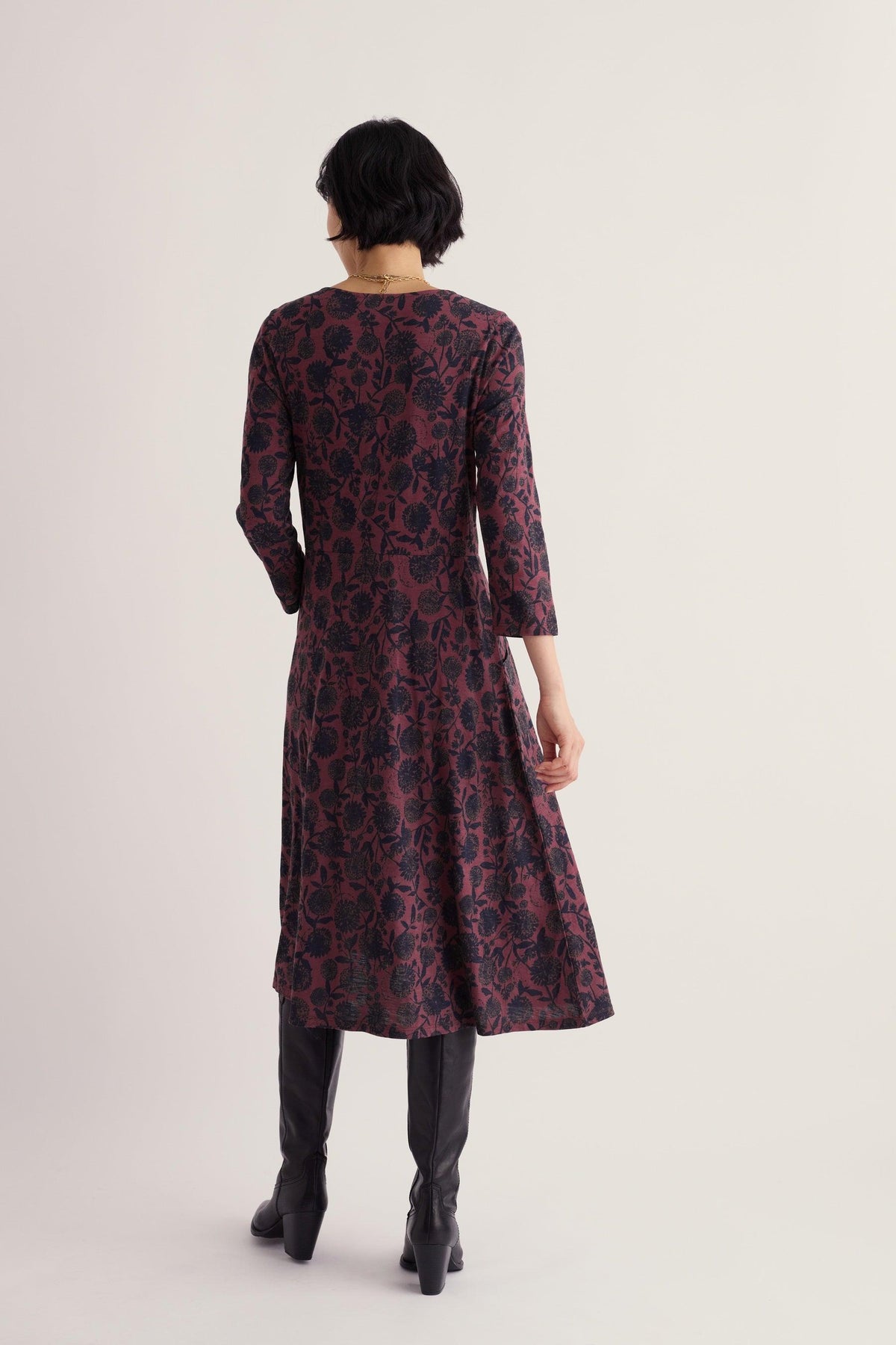 Woman seen from behind wearing a purple plum floral casual dress with 3/4 length sleeves and black boots.