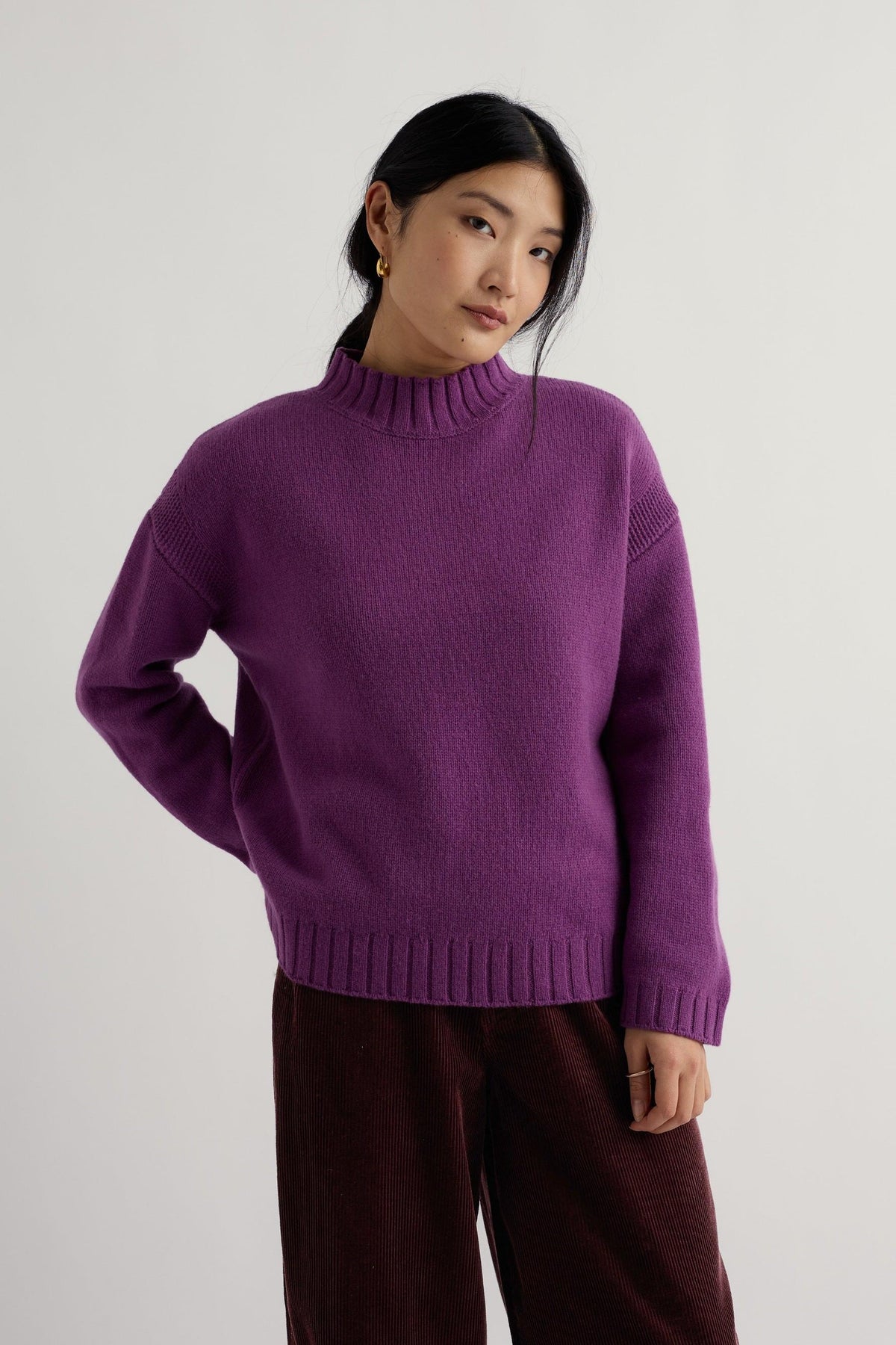 A young woman wearing a purple knit jumper against a plain light background.