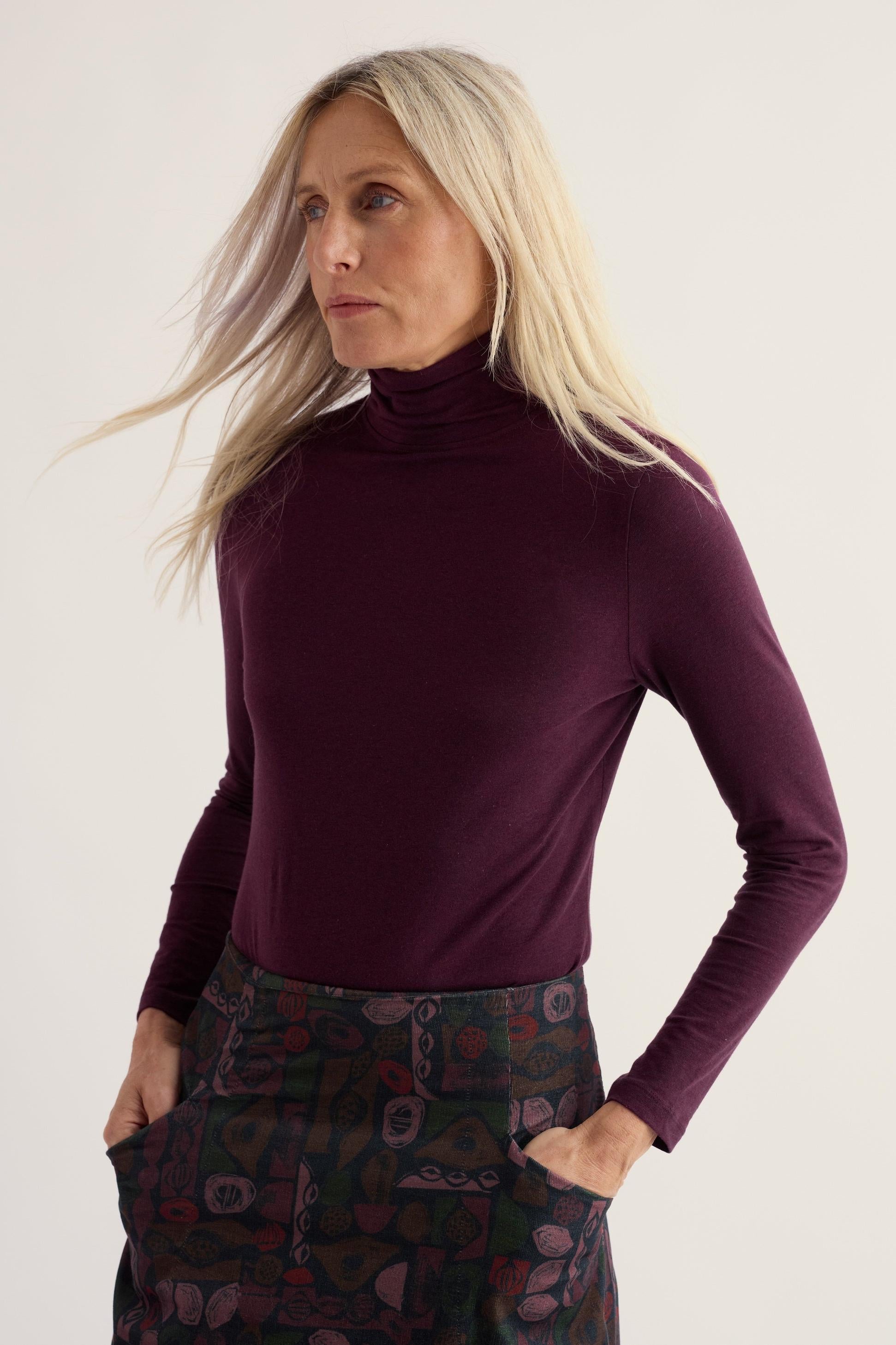 Woman wearing a purple organic cotton roll neck top against a plain background
