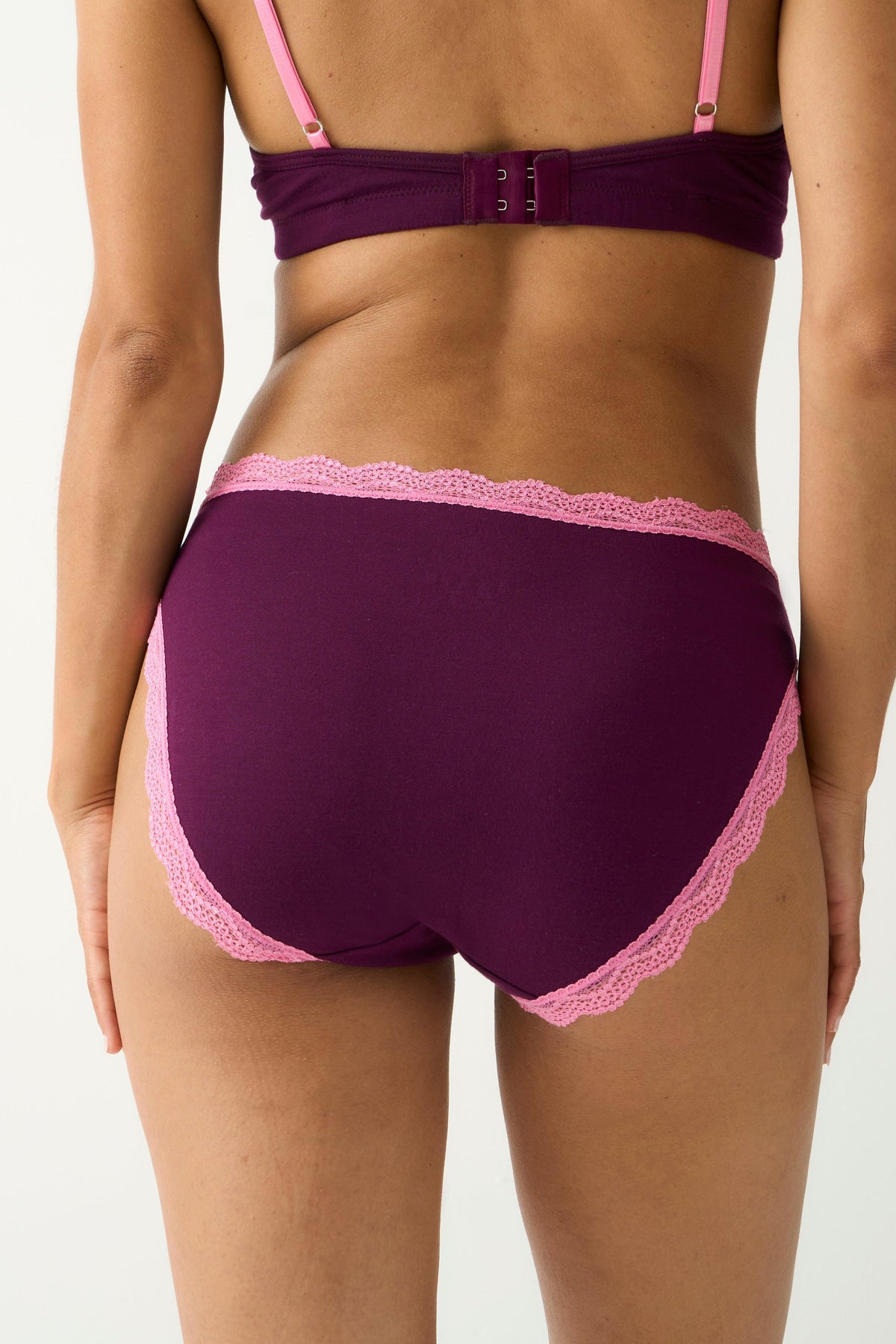 Rear view of a woman wearing purple classic cut underwear with pink lace trim and a matching bra.